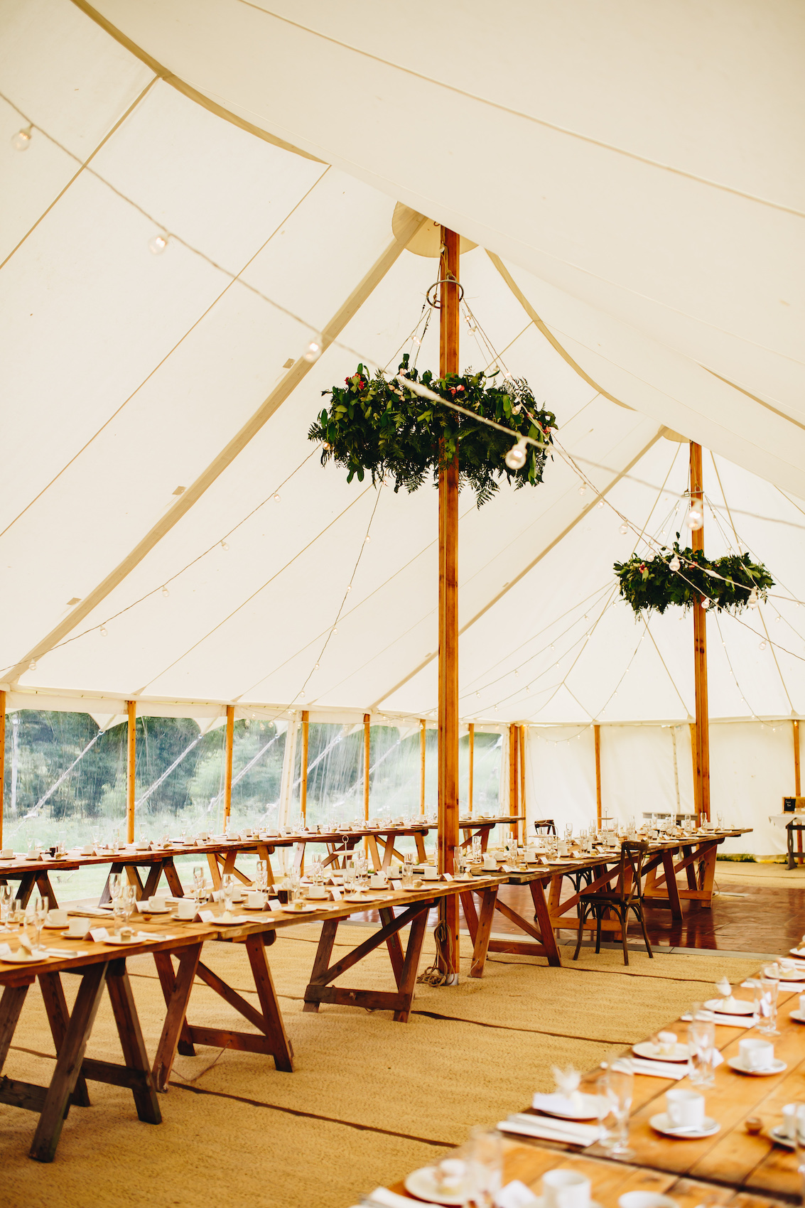 Long banquet tables in a large marquee with floral halos around the posts