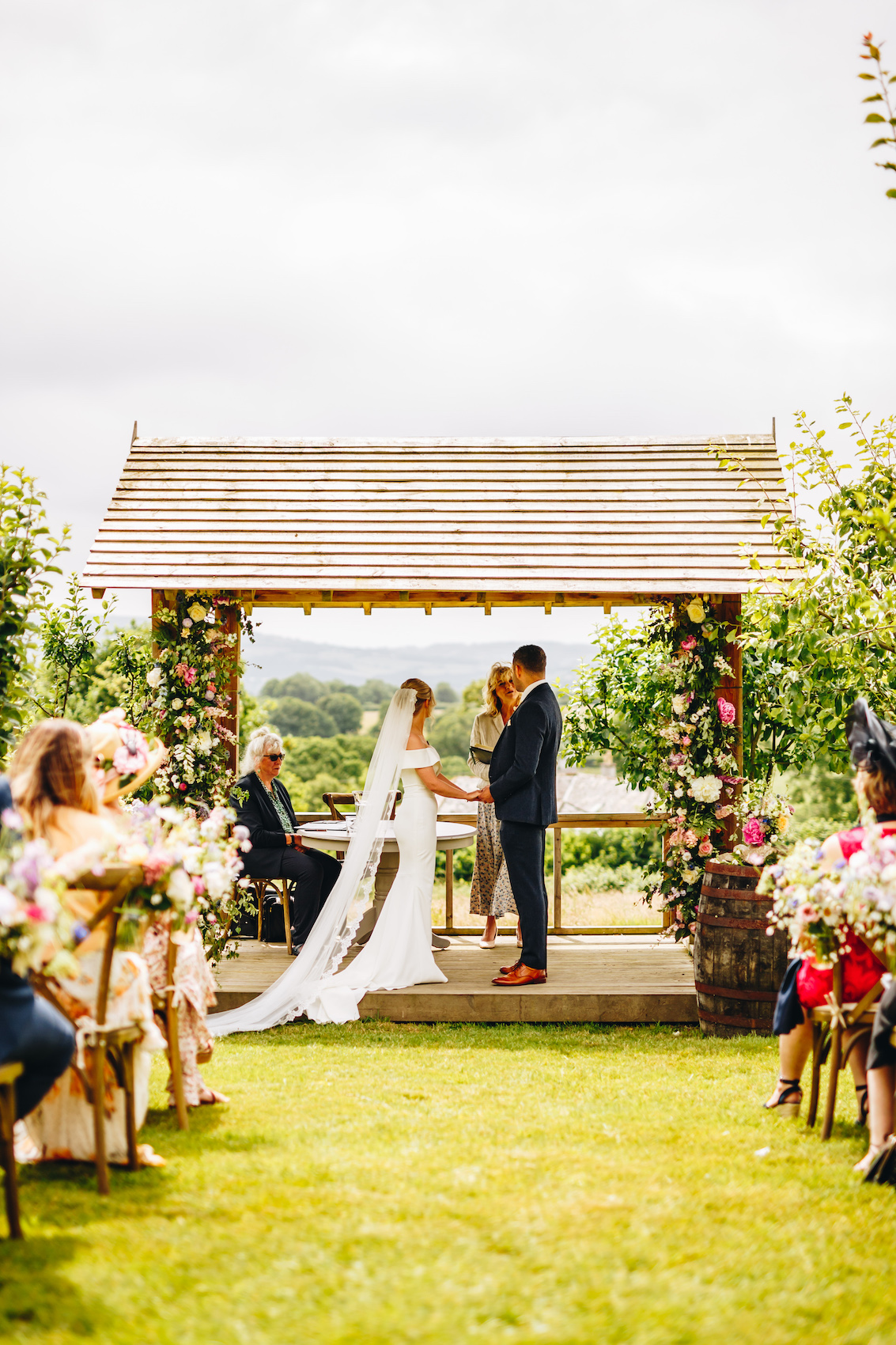 Bride and groom in a wooden pergola with flowers all over it, getting married