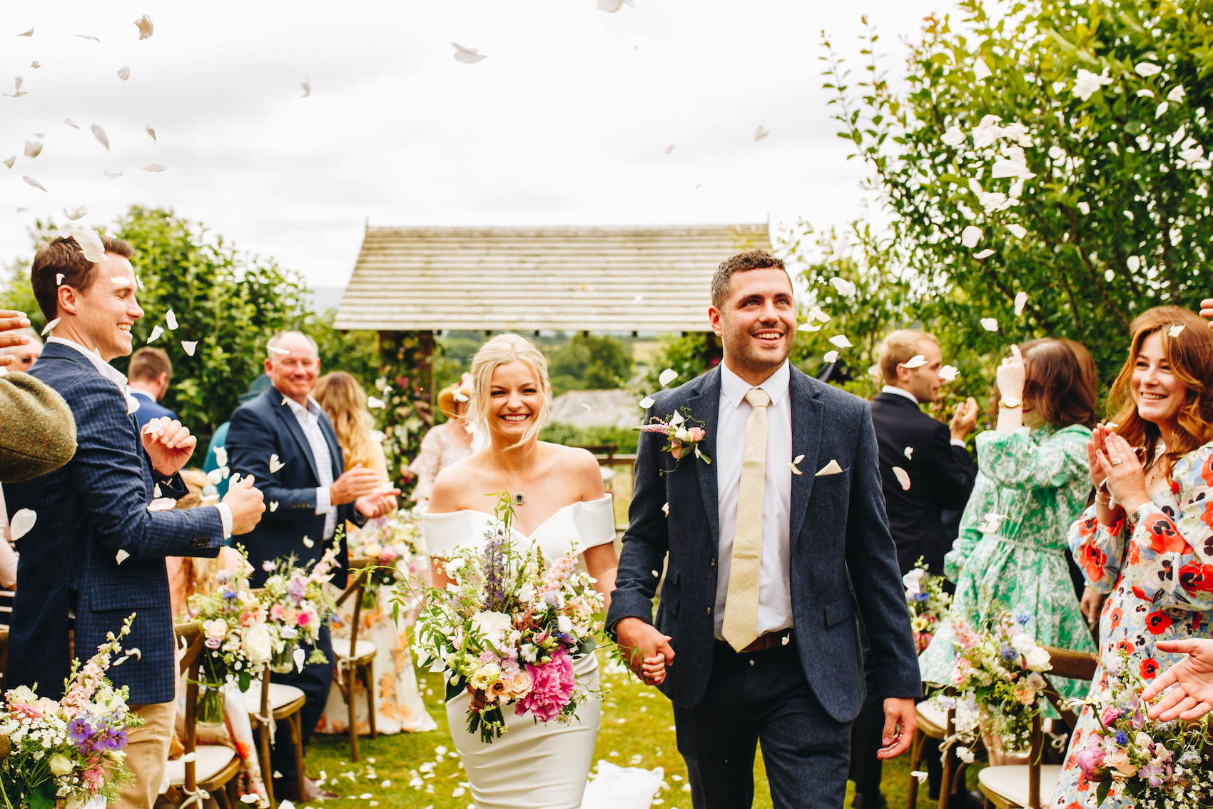 Bride and groom walk up the aisle with confetti in the air