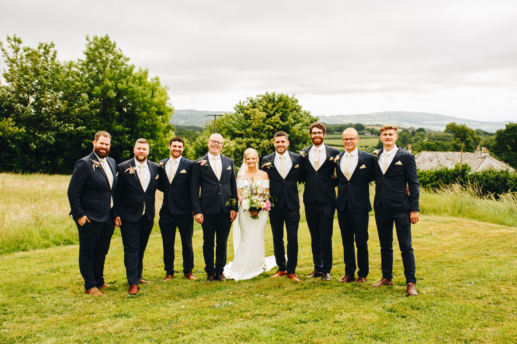 Bride and groom smiling with the groomsmen in a field with the valley in the background
