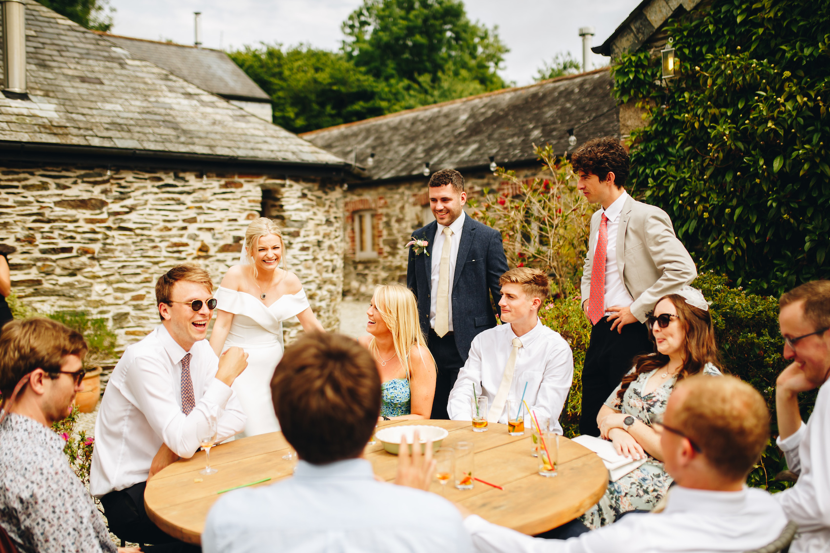 Bride and groom with guests all chatting around a table in a gravel courtyard with old brick farmyard buildings