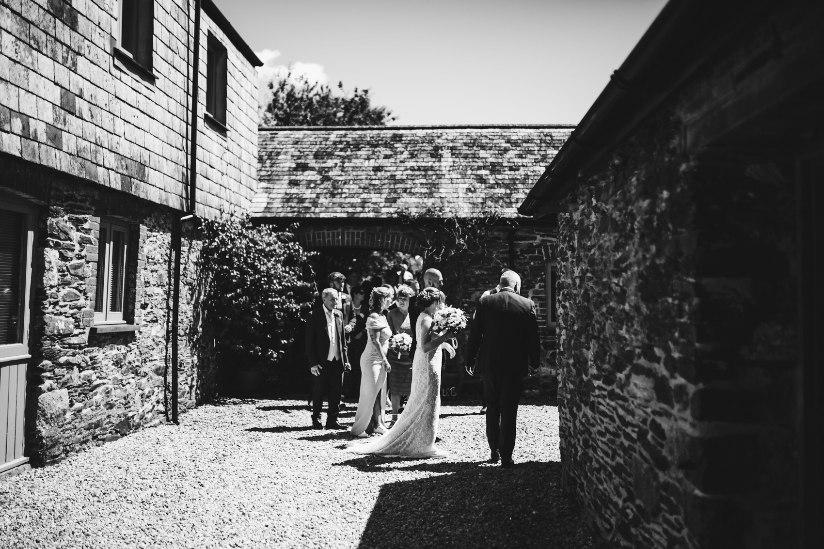 Black and white photo of bridal couple leading the procession from ceremony to reception, through a courtyard past bricked buildings