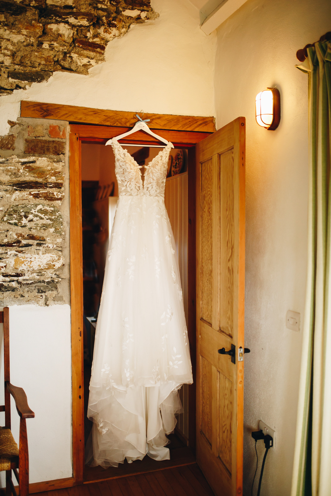 Wedding dress hanging up in a doorway, with a wooden door and brick surround