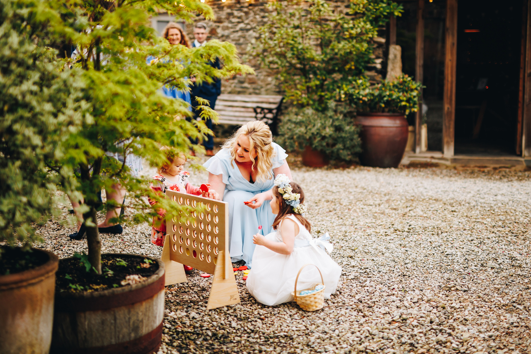 Close up of bridesmaid and her daughter playing garden games in a courtyard surrounded by potted plants and trees