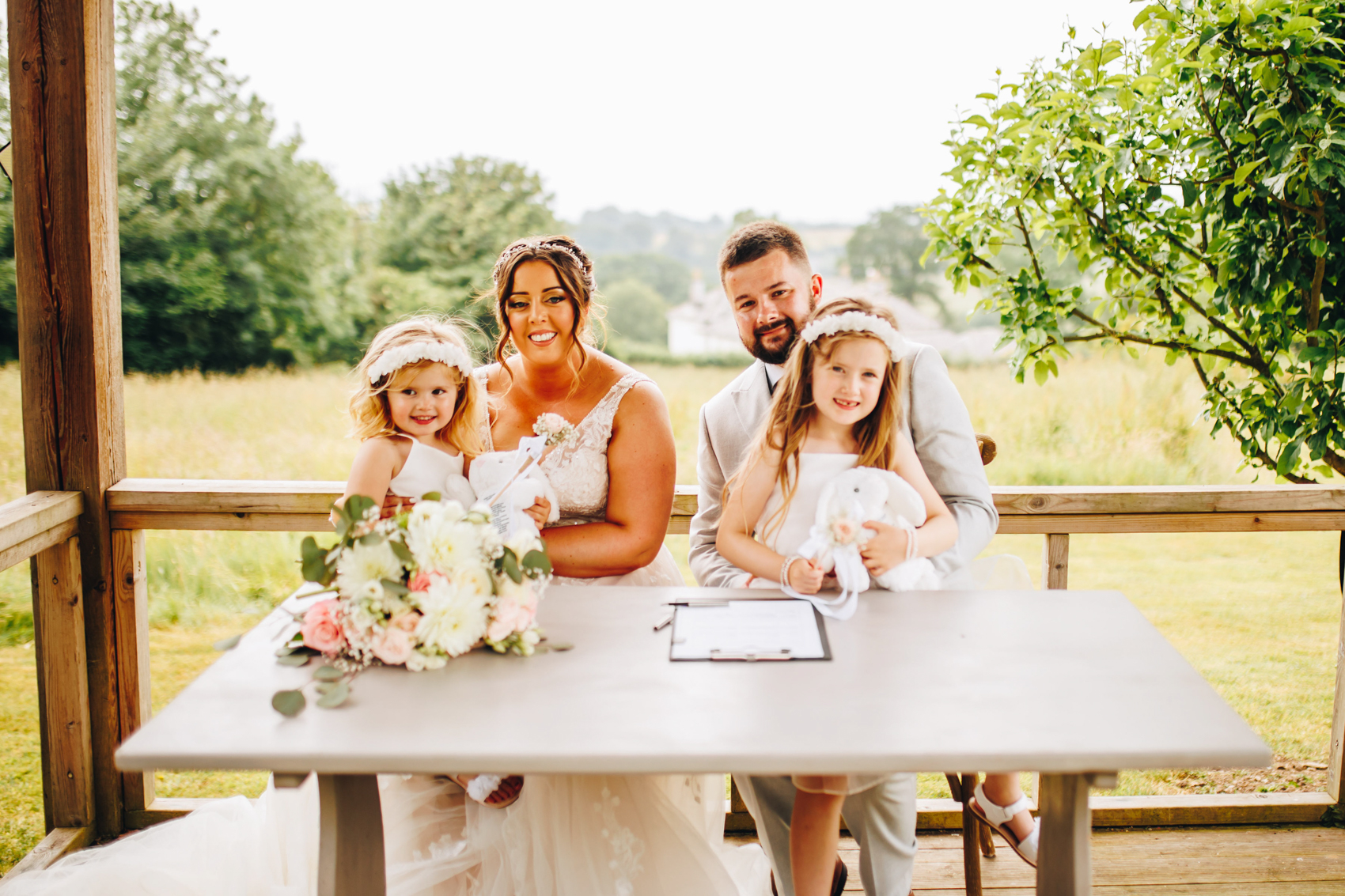 Bride, groom, and their two daughters sat smiling at the signing table after signing the register