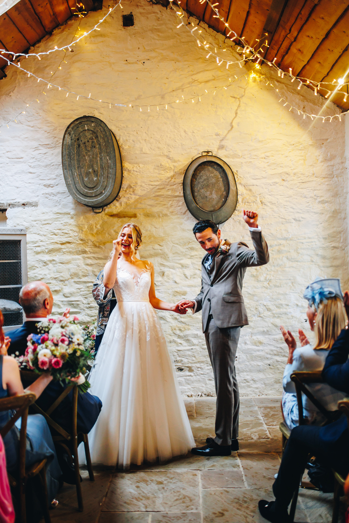 The bride and groom celebrating getting married with their hands in the air as their guests clap
