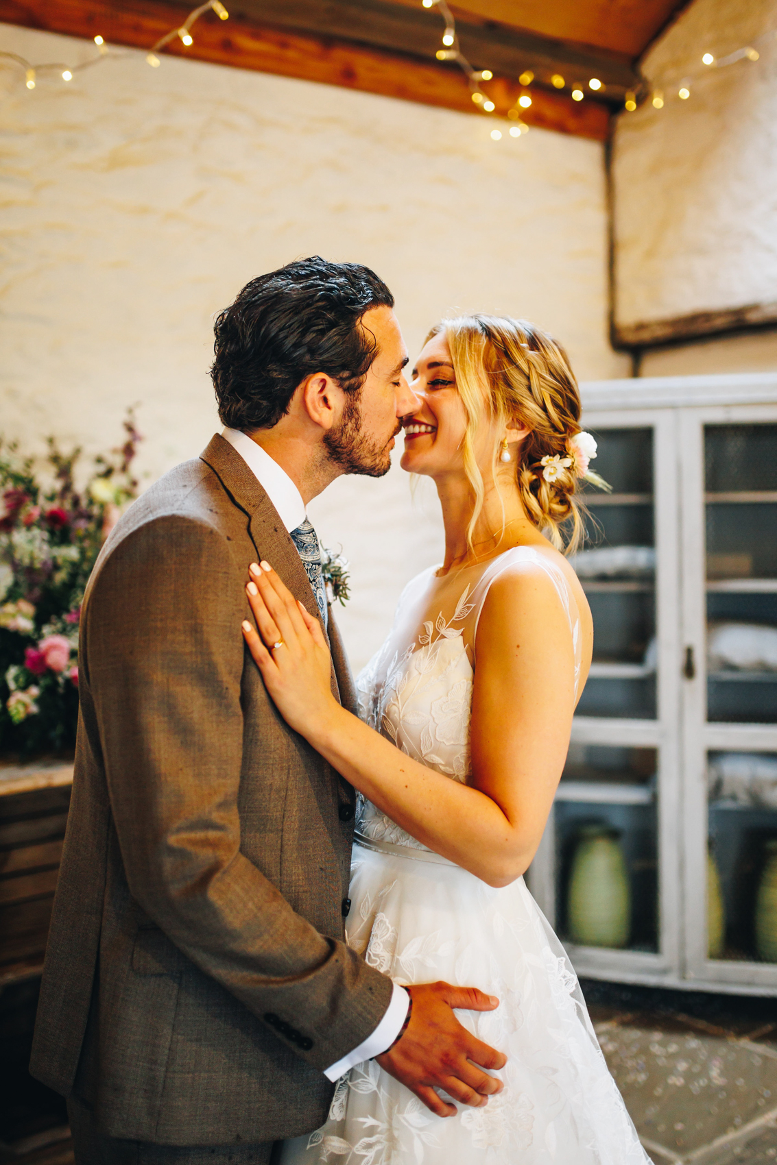 A couple kissing in a cute barn room with fairy lights in the background