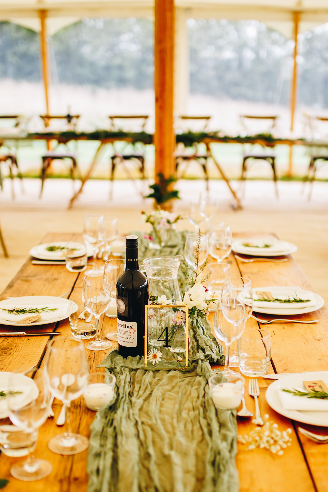 Close up of table set up - green table runners, a "4" in a gold frame, glasses and a bottle of bubbly on a long table