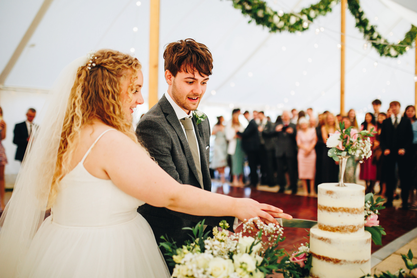 Bride and groom cut their wedding cake while their guests watch on