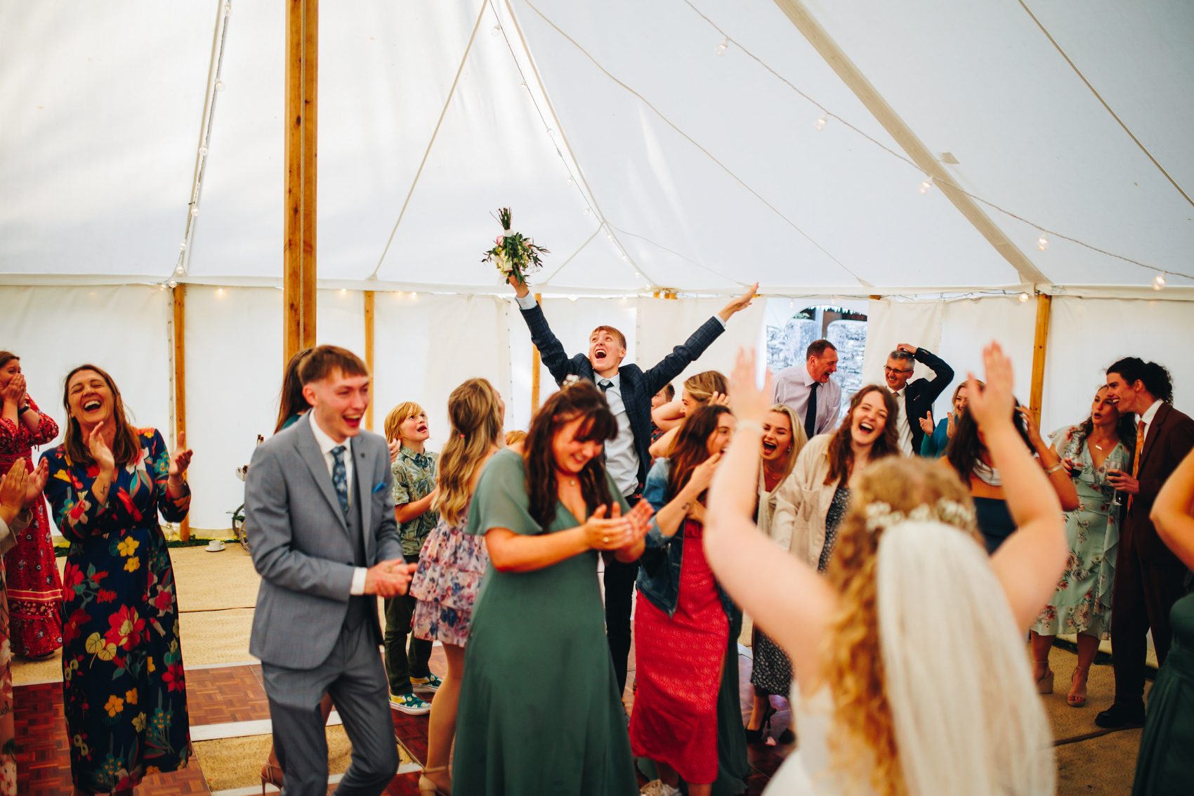 Bride's cousin leaps into the air to catch the bouquet, arms stretched out, while the other trying to catch it laugh in defeat