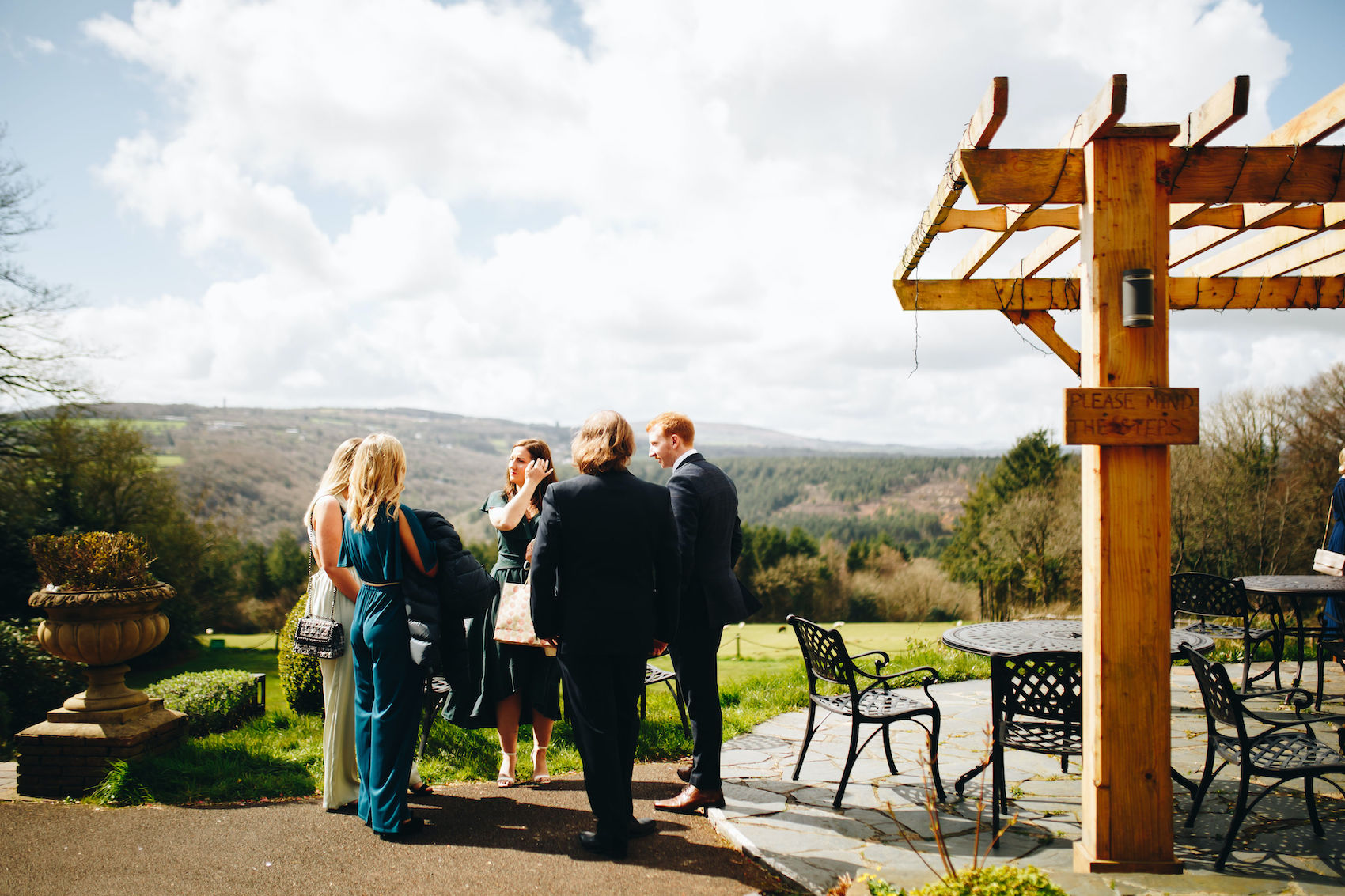 Couple's friends wait for the ceremony, stood by the patio overlooking the valley