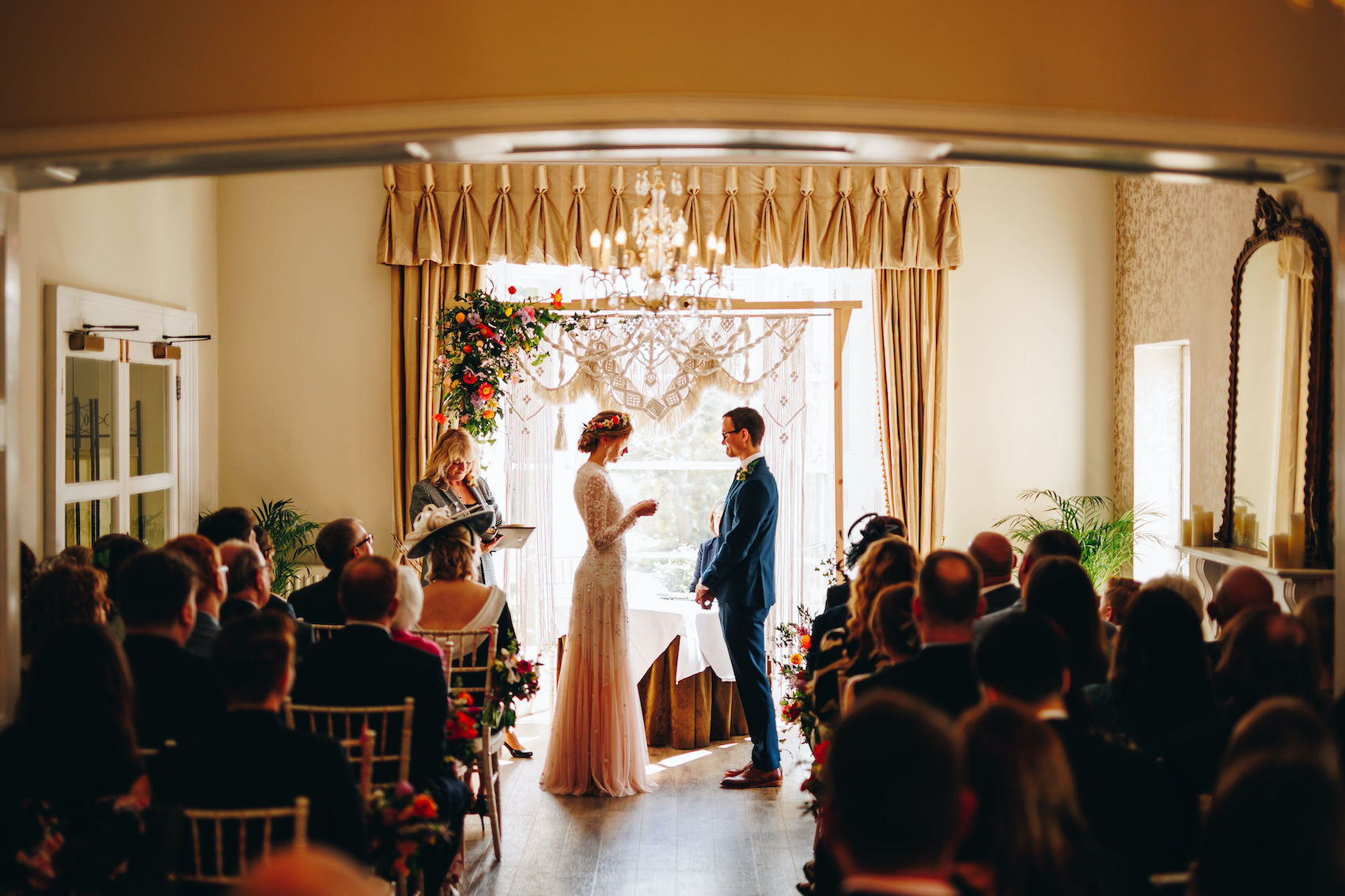 Bride reads out her vows to her husband in front of a macrame frame with florals.