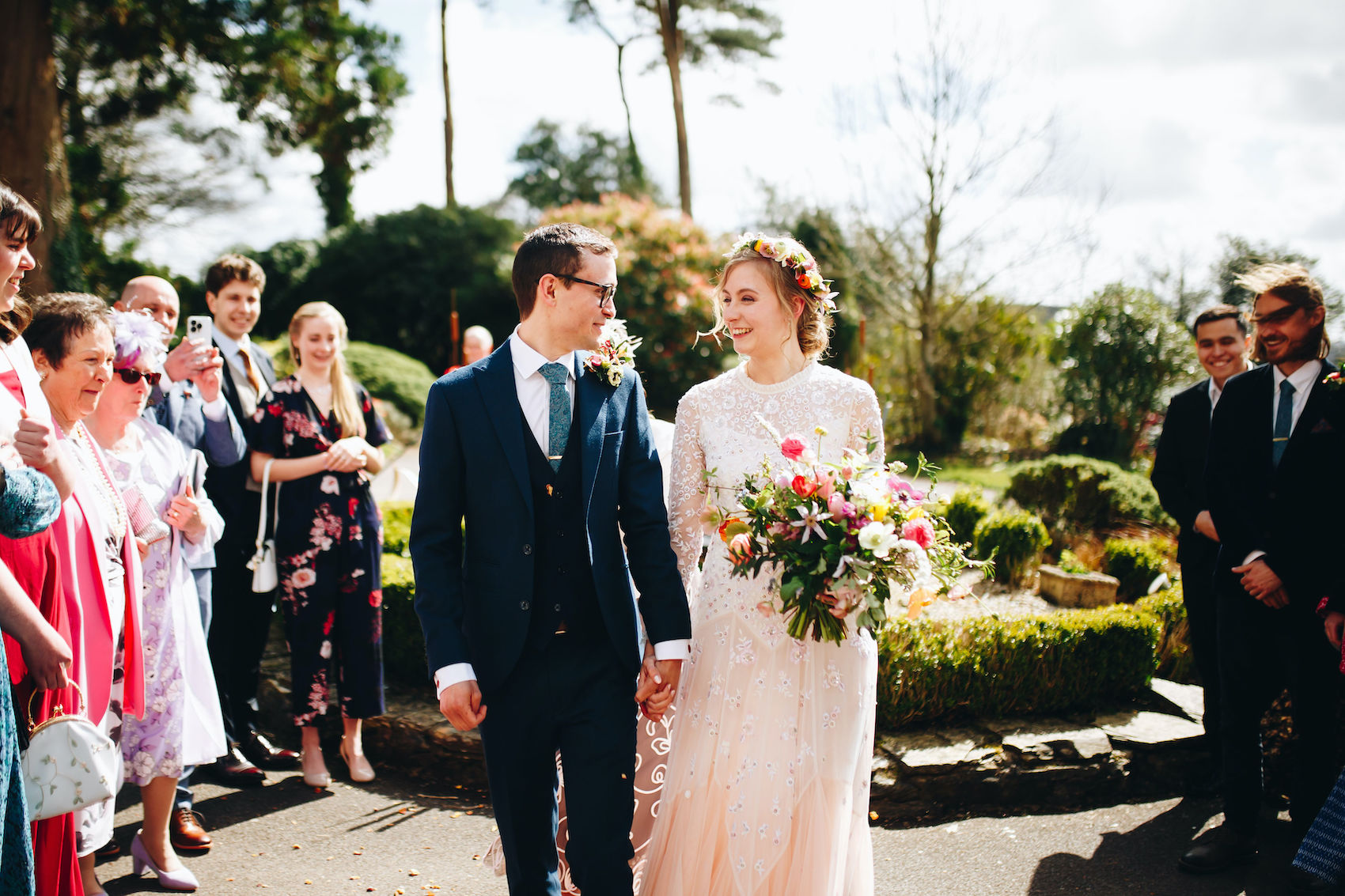 Bride and groom smiling after having confetti thrown at them, surrounded by their guests
