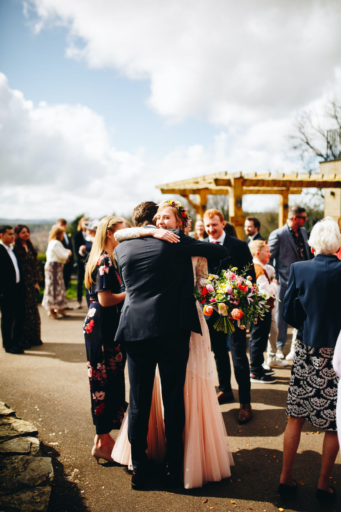 Bride in pale pink dress hugs guests while holding a beautiful big bouquet