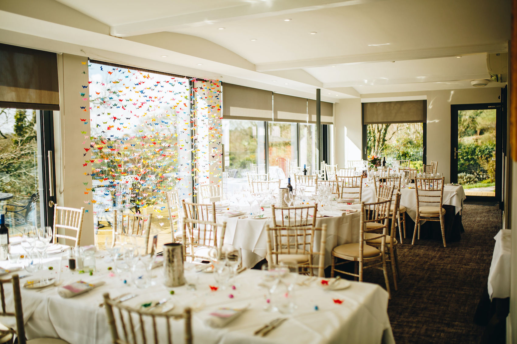 Photograph of room all set up for wedding reception, with table-clothed tables and white wooden chairs