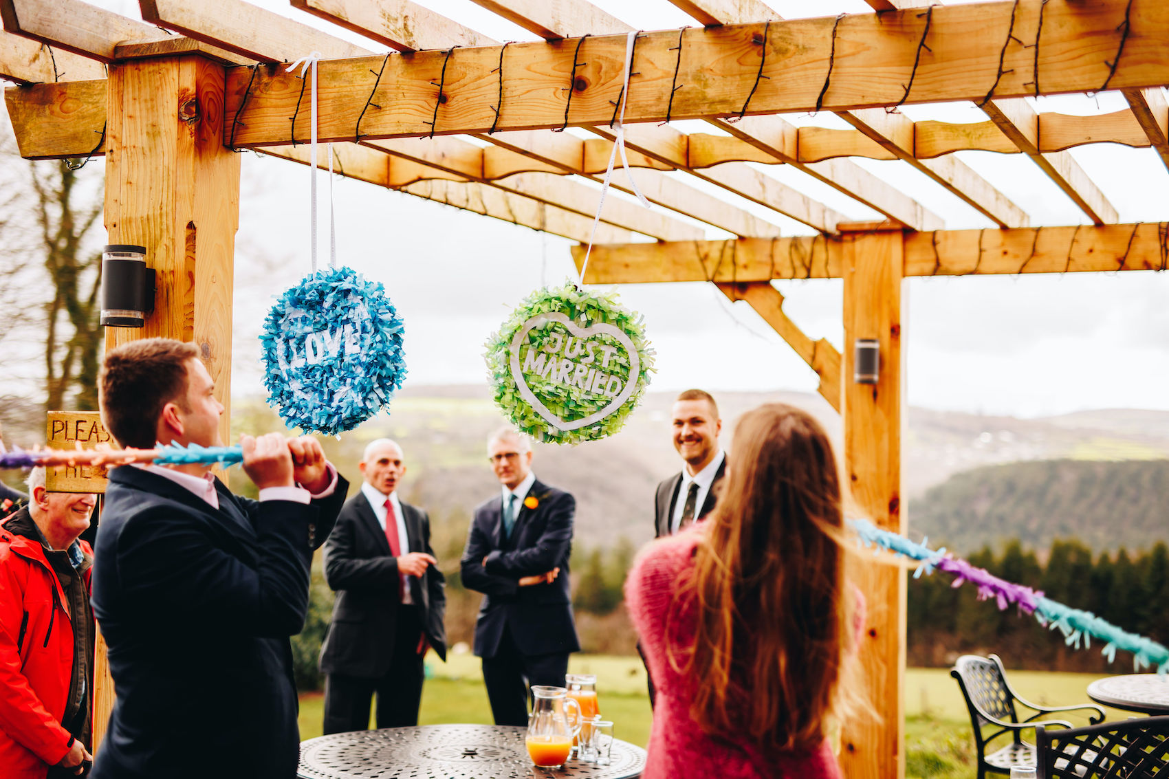 Guests hitting the handmade piñatas saying "LOVE" and "JUST MARRIED", hanging from a wooden veranda