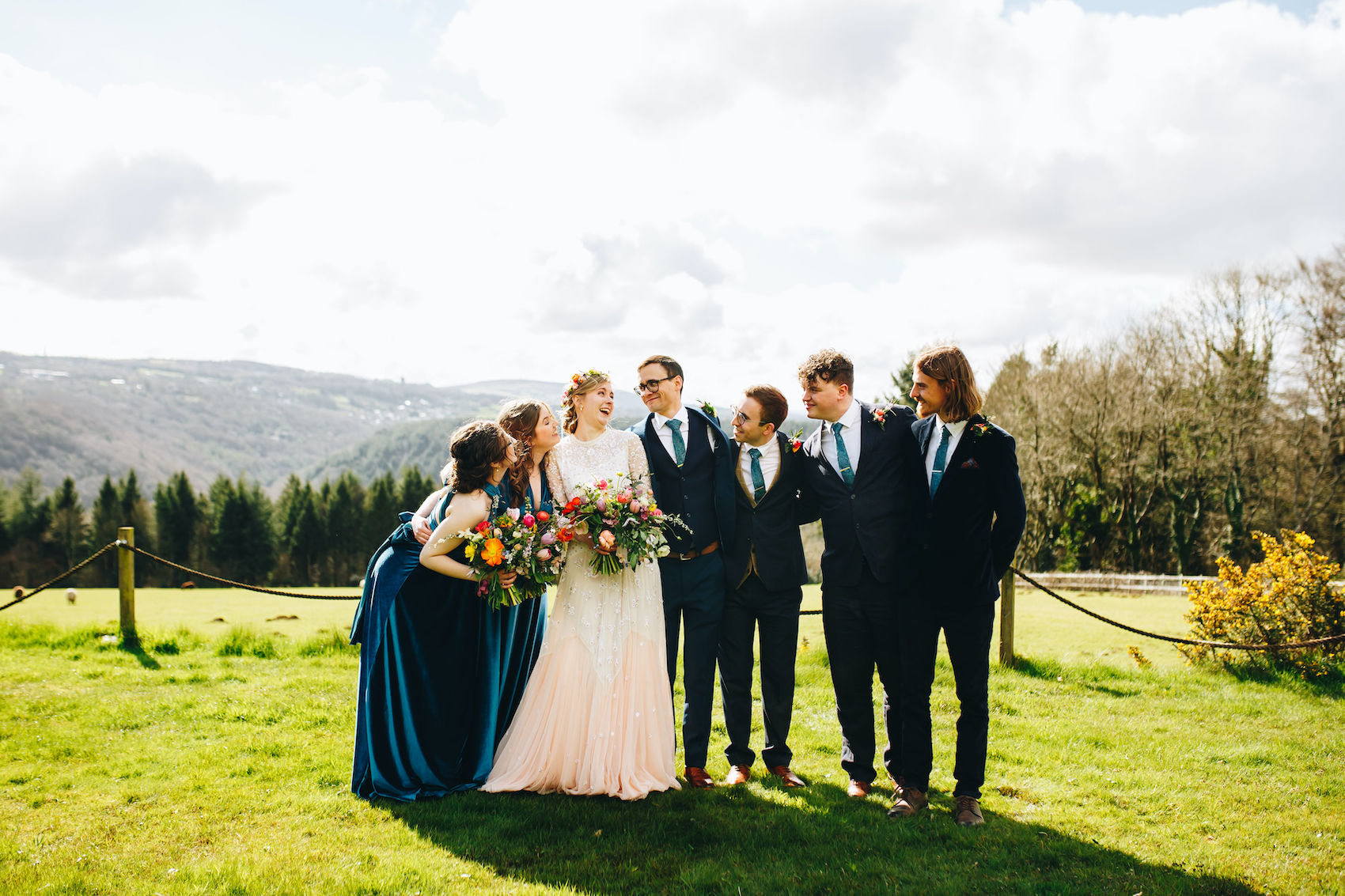 Bride, groom and bridal party all huddle in and look at the newlyweds in the evening sun