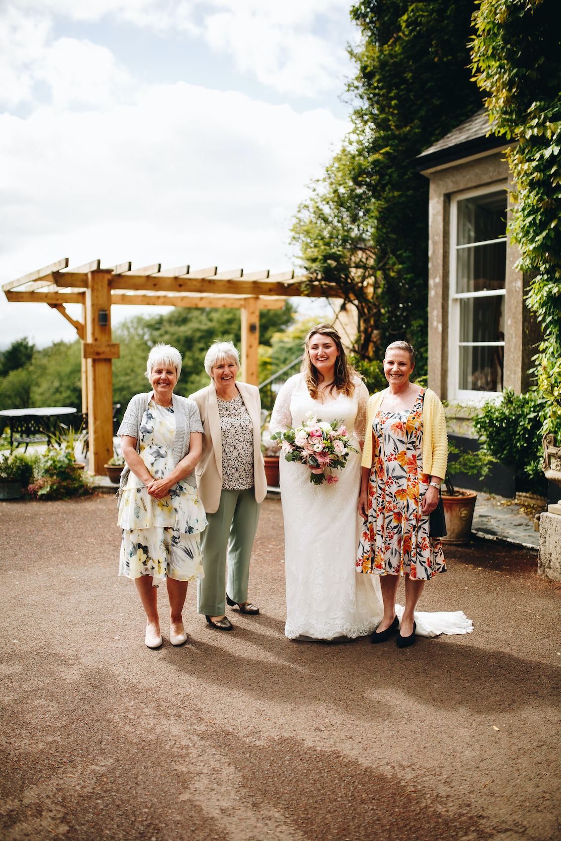 Bride stands with aunts in front of Manor Home, all smiling