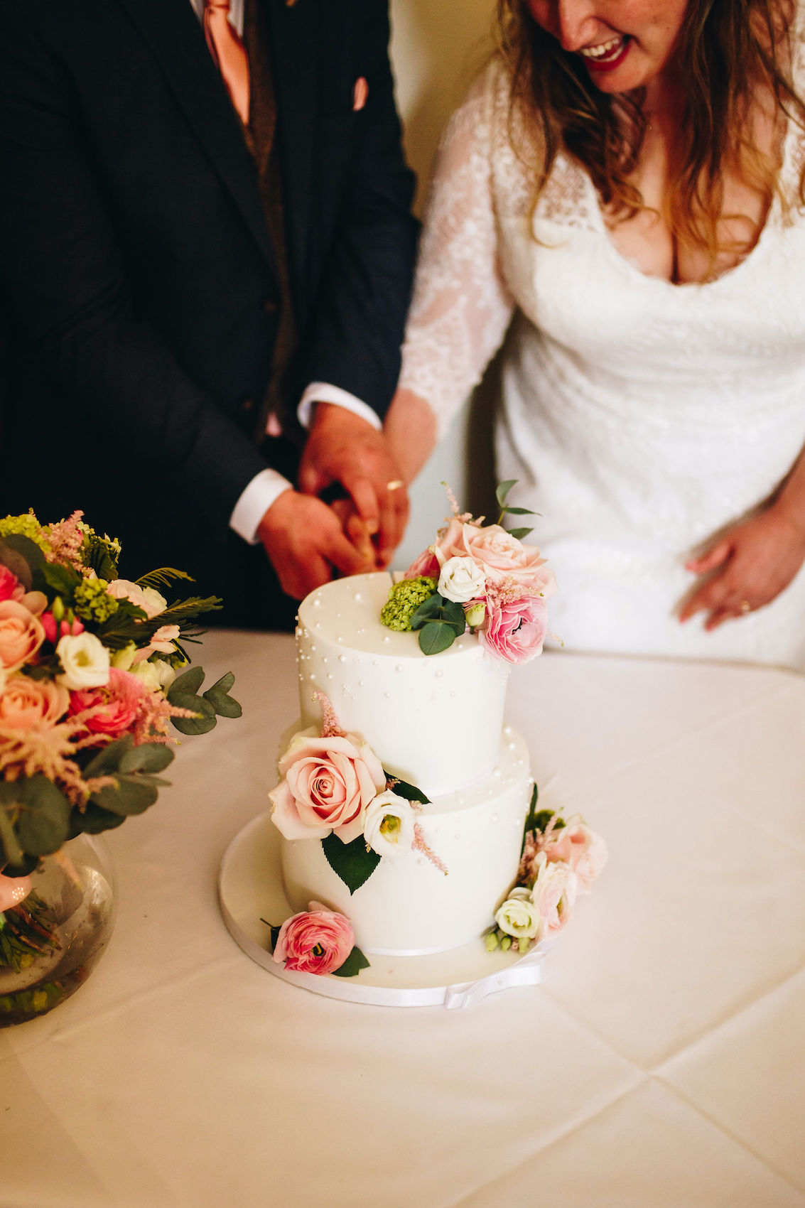 Bride and groom cutting their wedding cake, cropped in to show the cake, their hands and arms and bodies but not heads