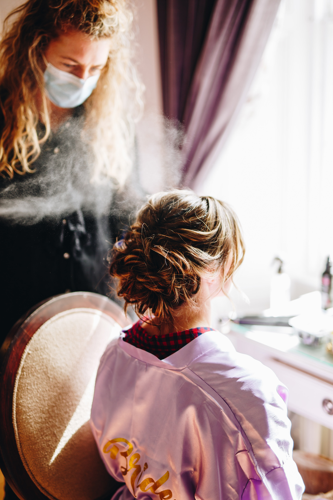 Photo of bride from behind as hairspray is sprayed on her hair