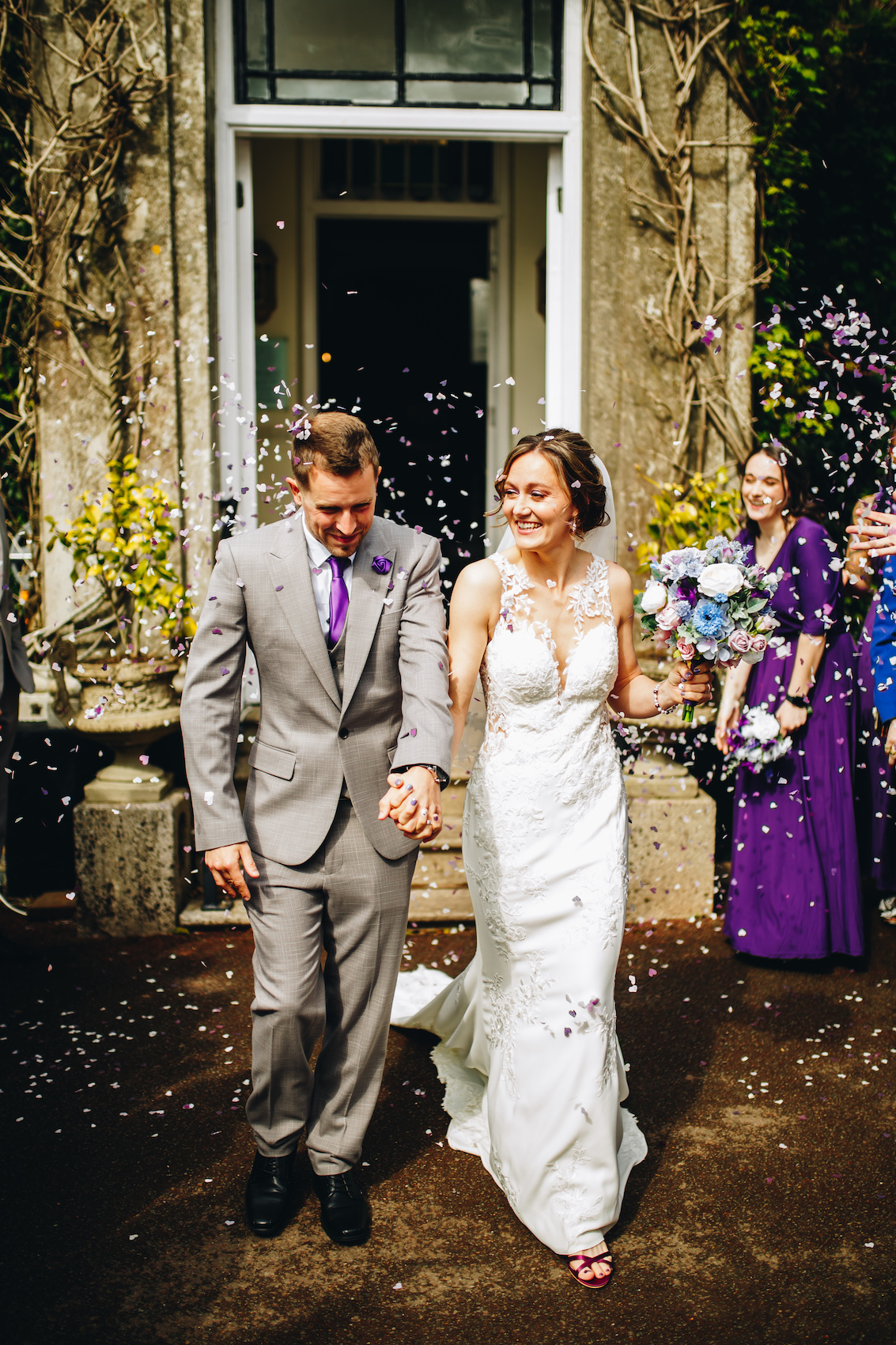 Bride and groom smiling as they walk out of the building into the shower of confetti