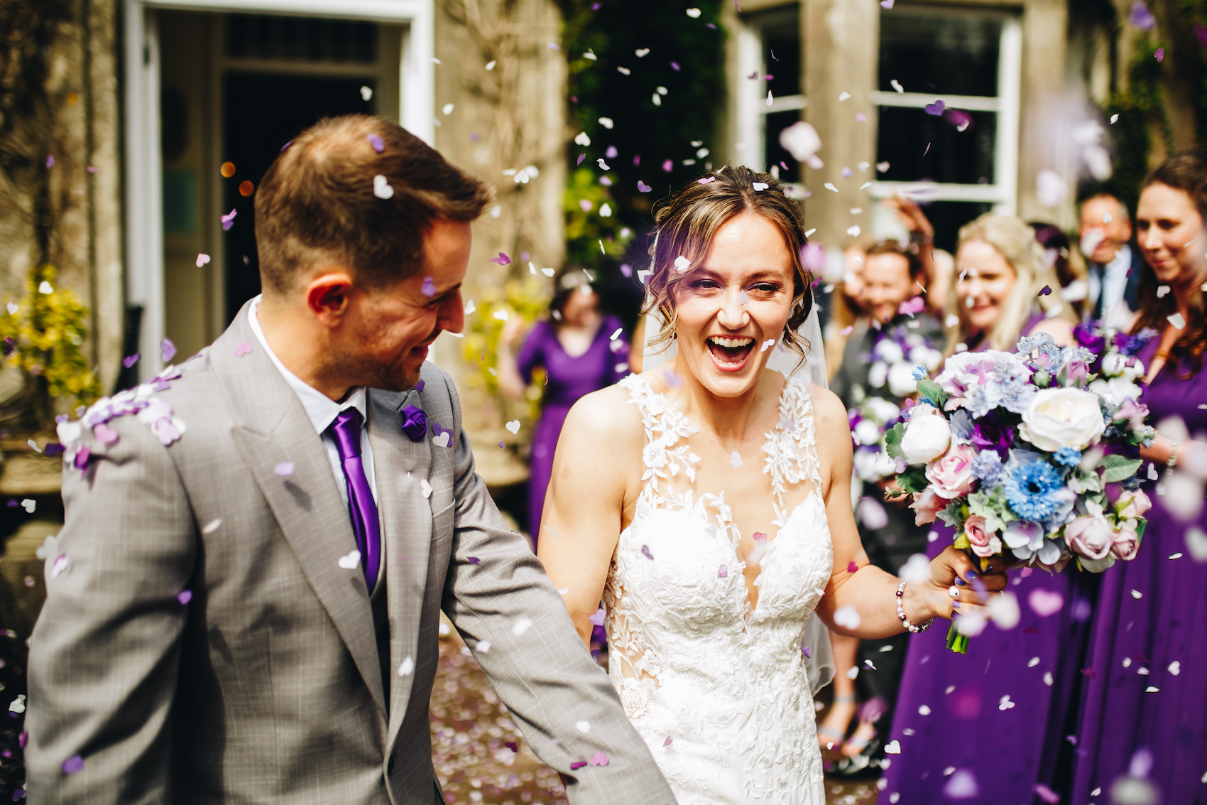 Bride and groom smiling as they walk out of the building into the shower of confetti