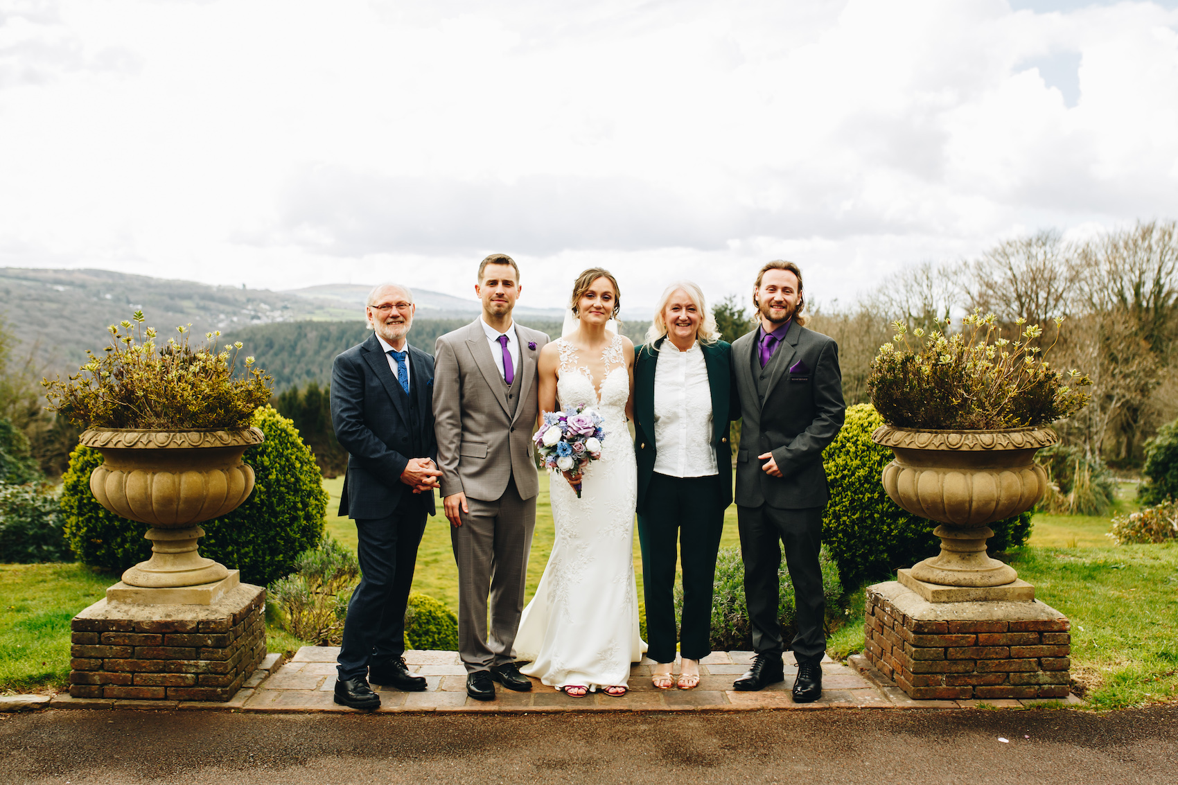 aBride and groom smile with family for a family group photo