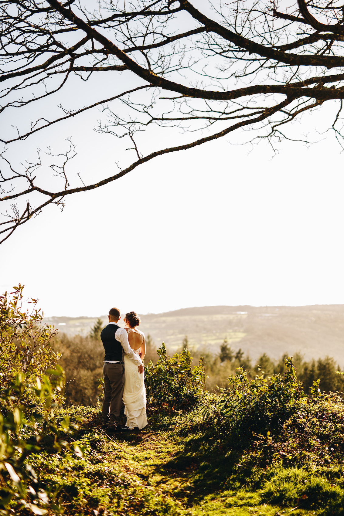 Bride and groom at sunset amongst the trees, looking out at the valley