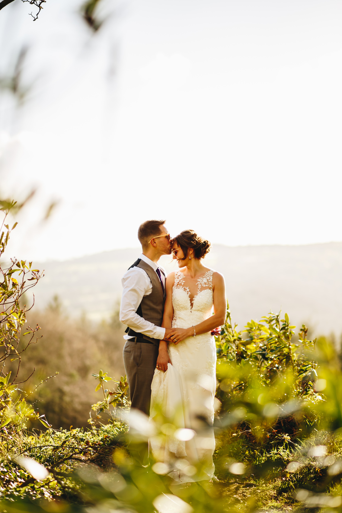 Bride and groom at sunset amongst the trees, he kisses her on the forehead
