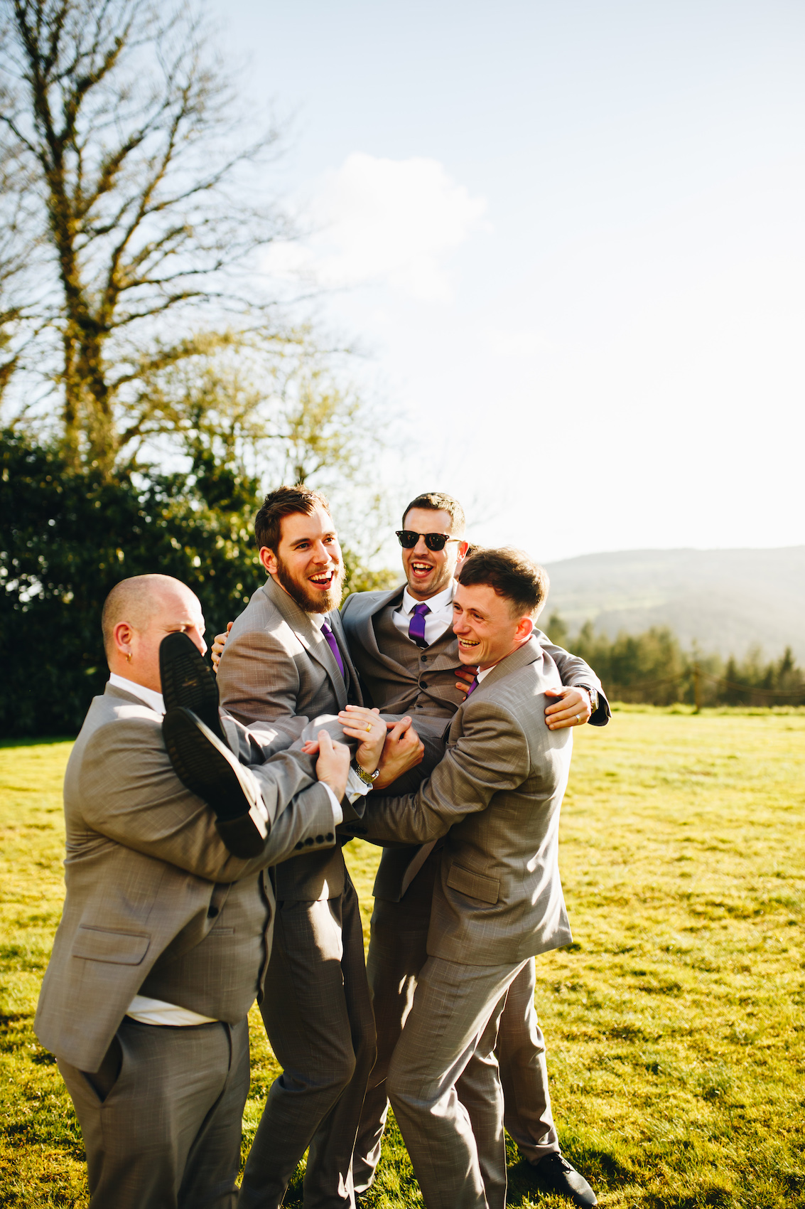 Groom is lifted into the air by his groomsmen on a grassy lawn
