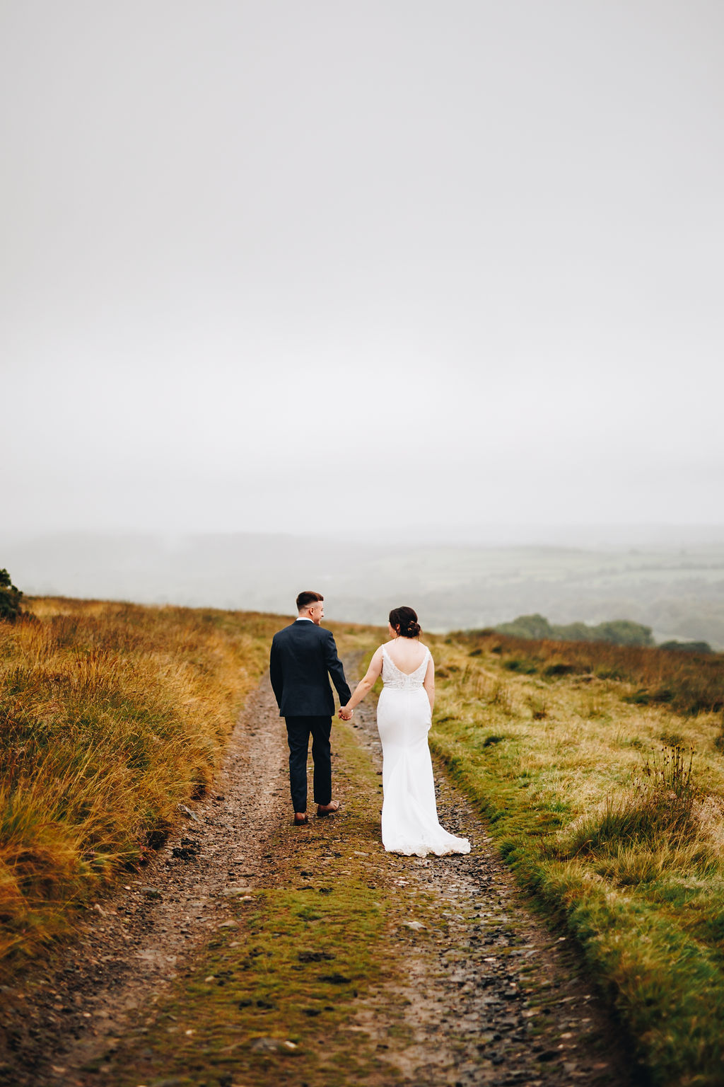 Photo of bride and groom walking away from the camera on a misty moorland track