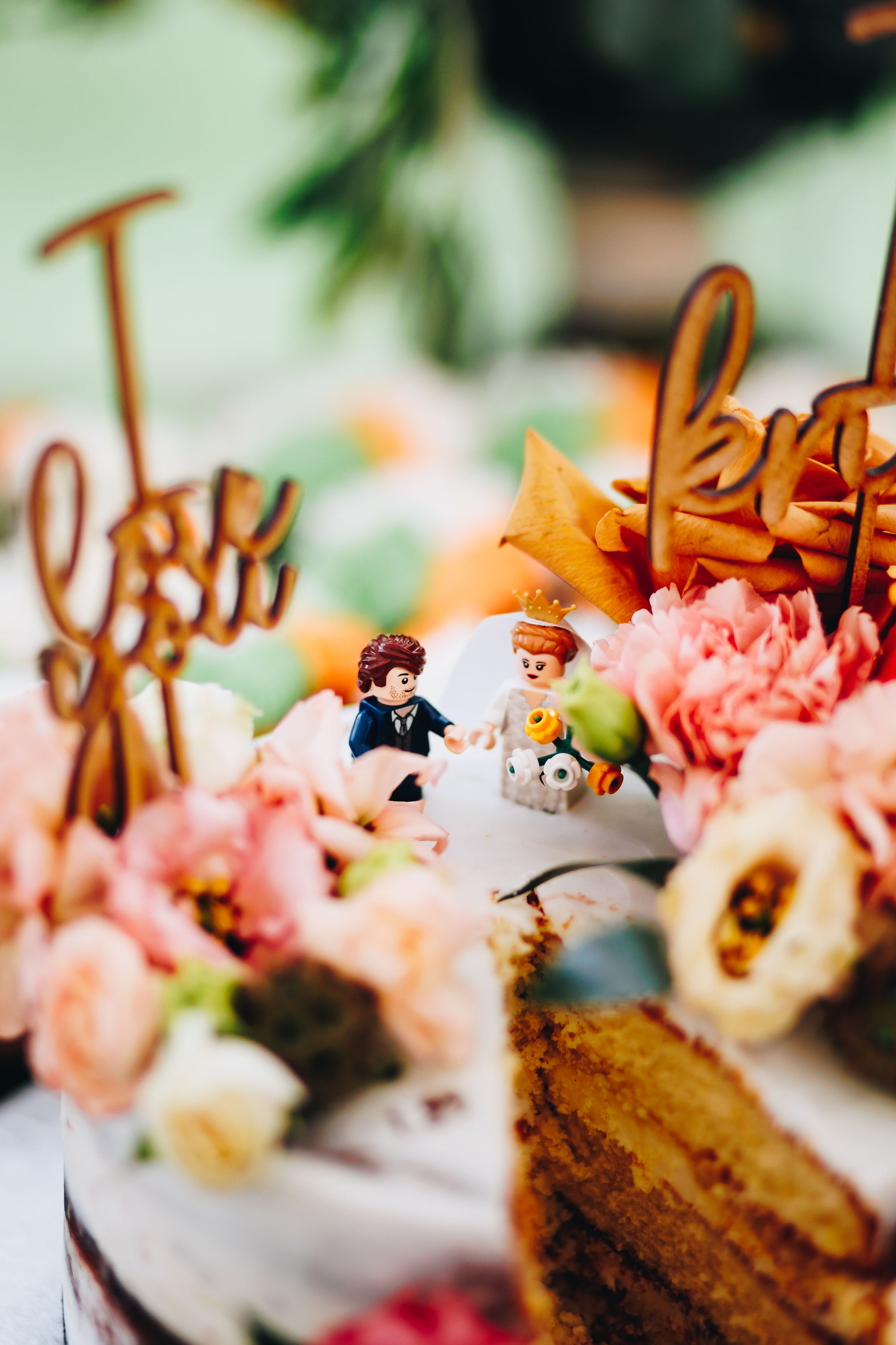 Close up of Lego cake toppers on wedding cake with flowers surrounding them