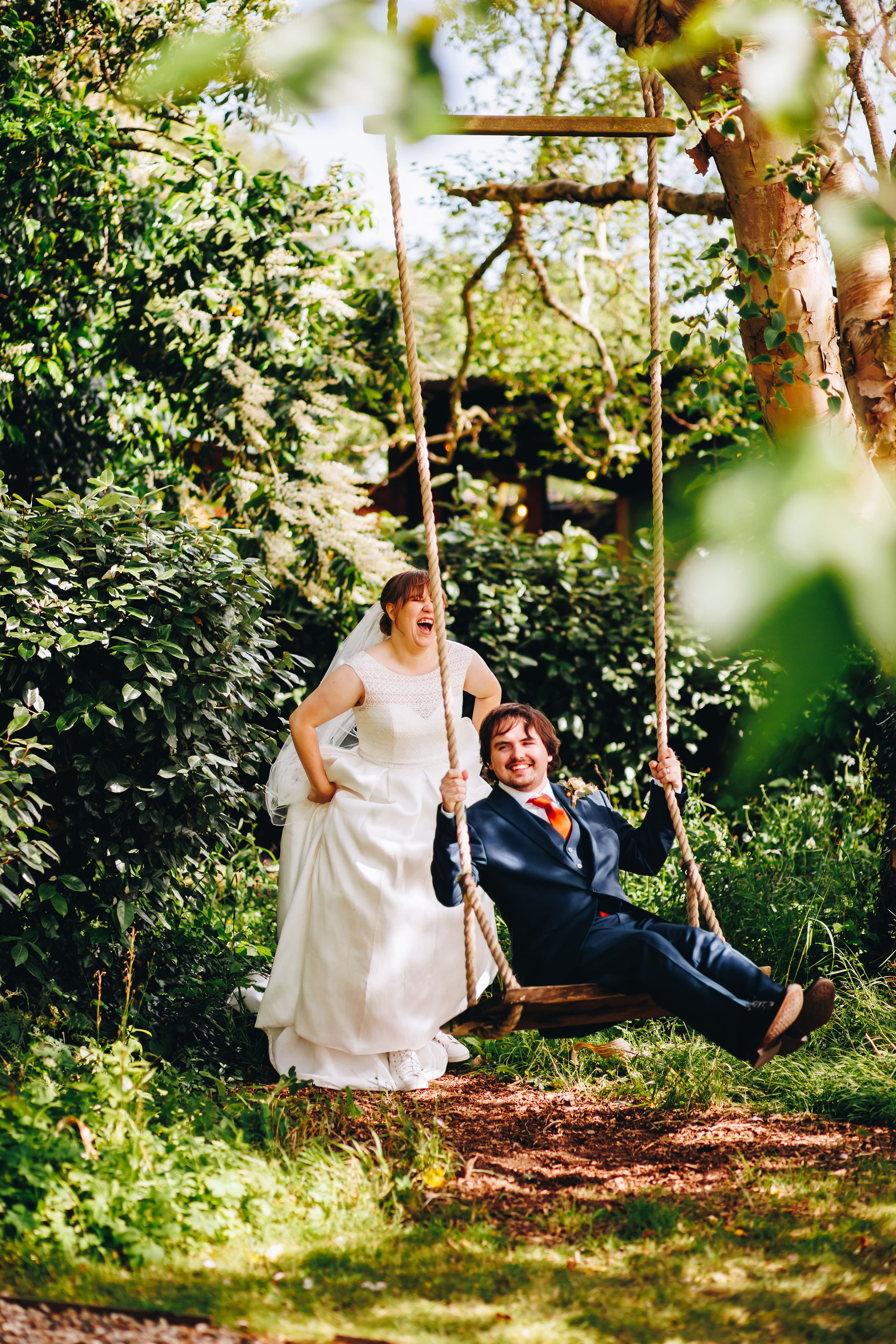 Bride laughs while pushing groom on a swing hanging in a tree