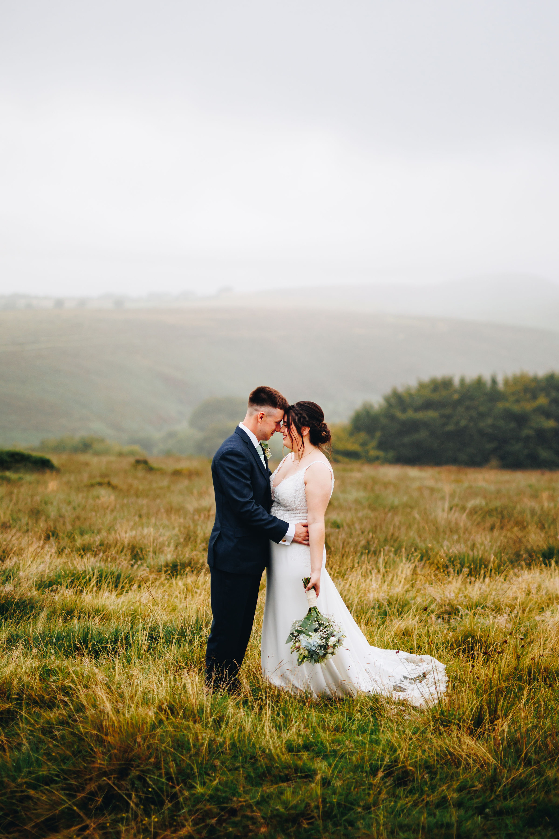 Bride and groom are forehead to forehead in a misty field in a valley