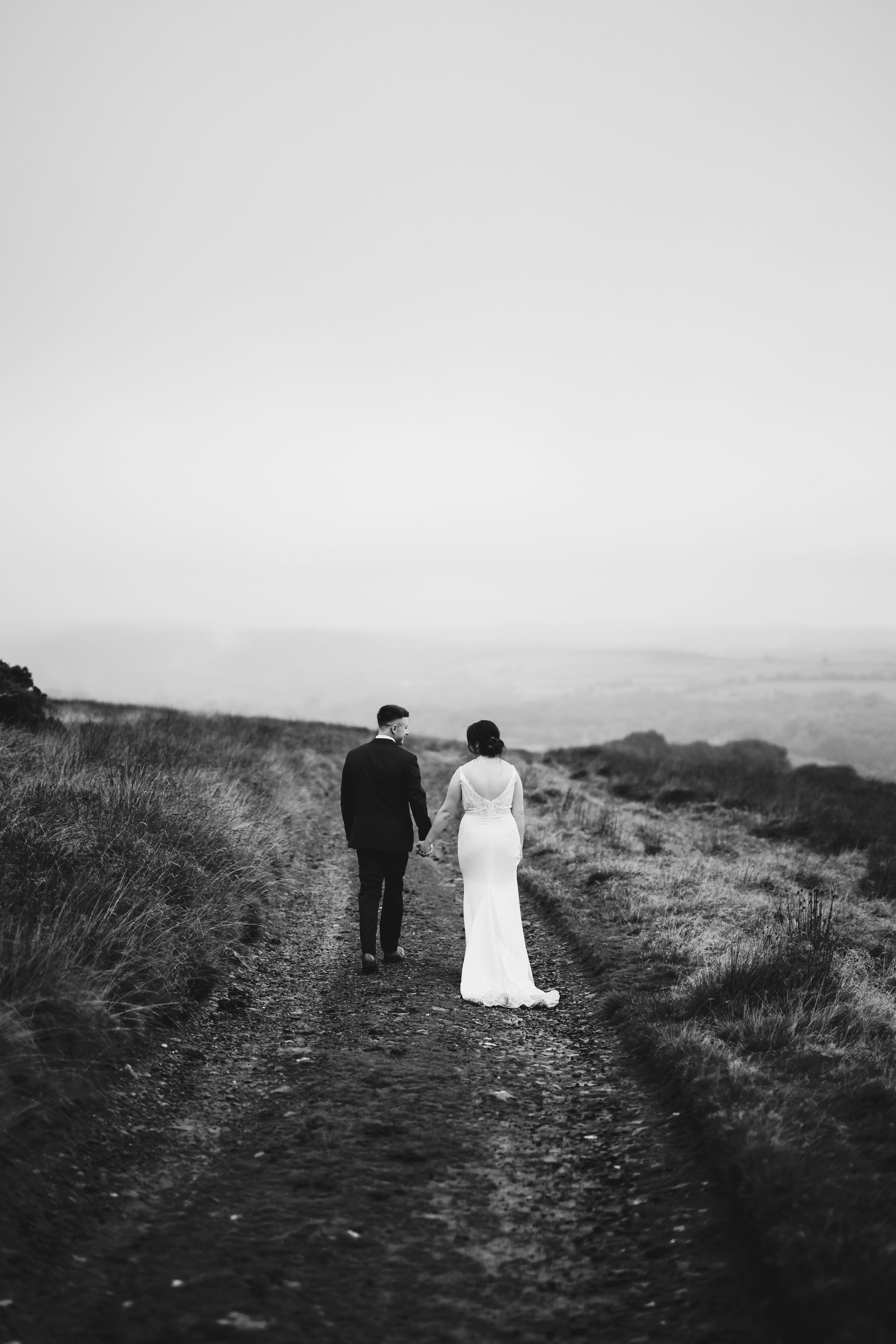 Black and white photo with couple walking down a track away from the camera