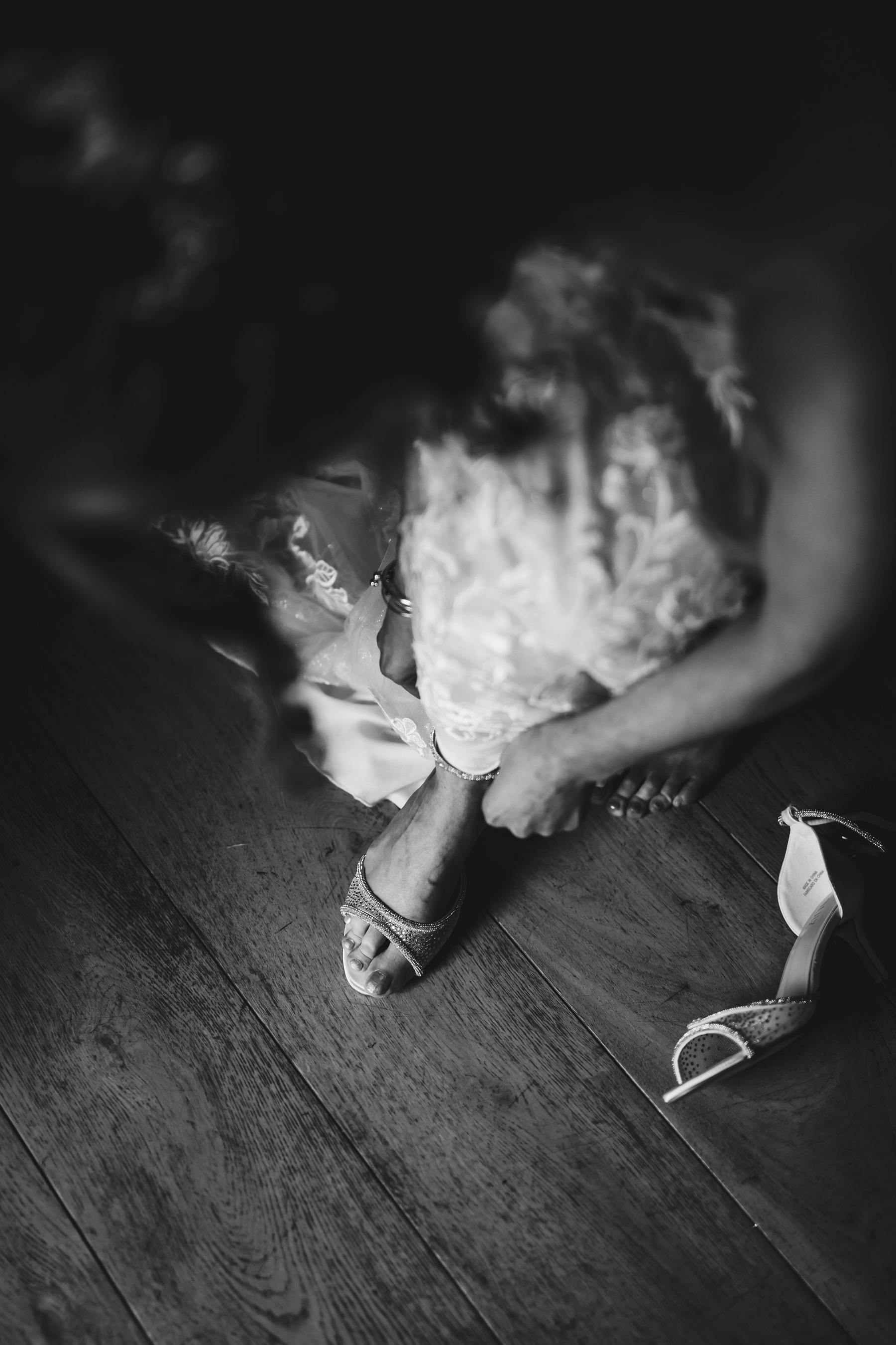 Black and white photo of bride doing up her wedding shoes
