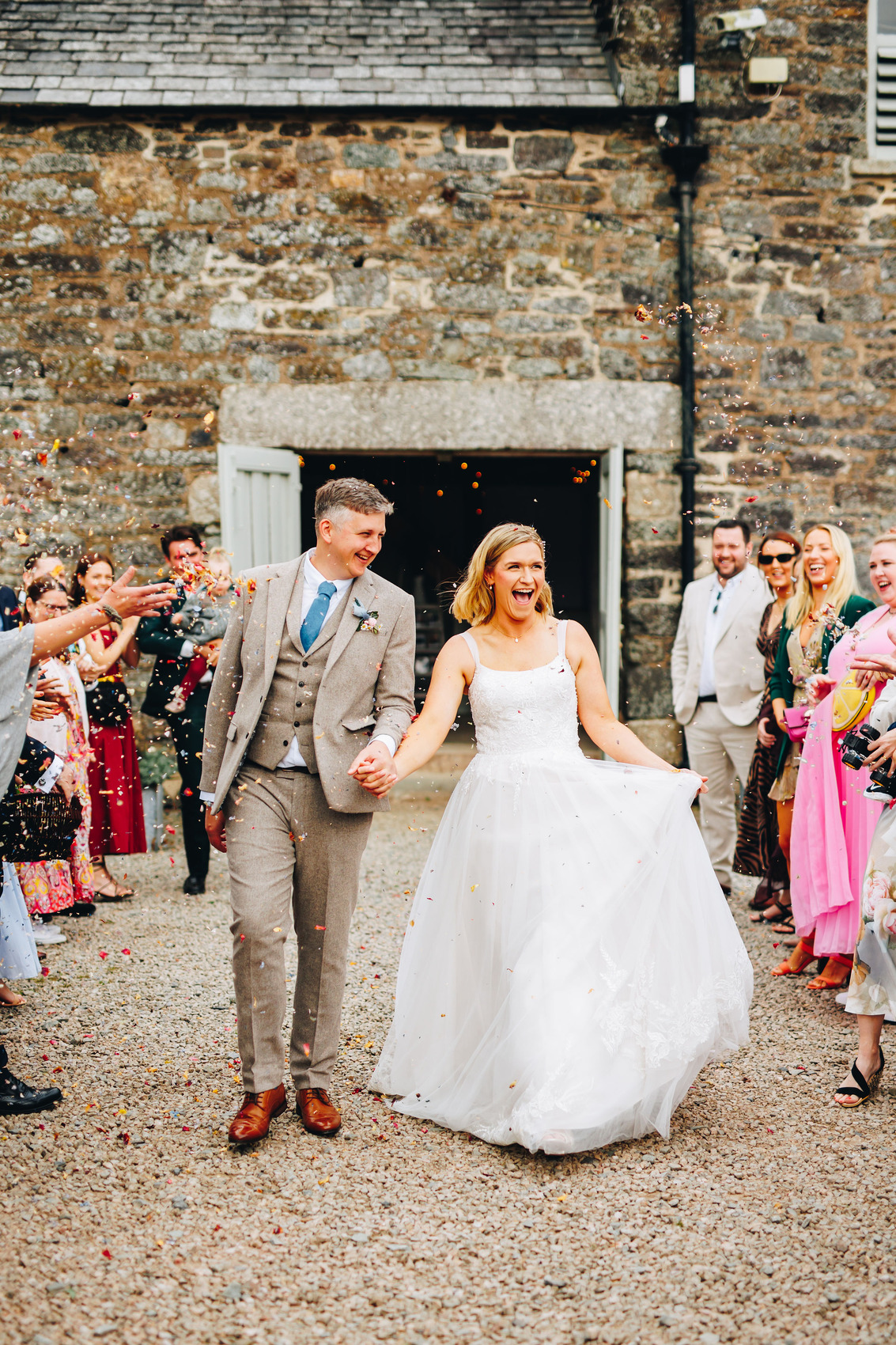 Couple excitedly walk the confetti line in front of a barn