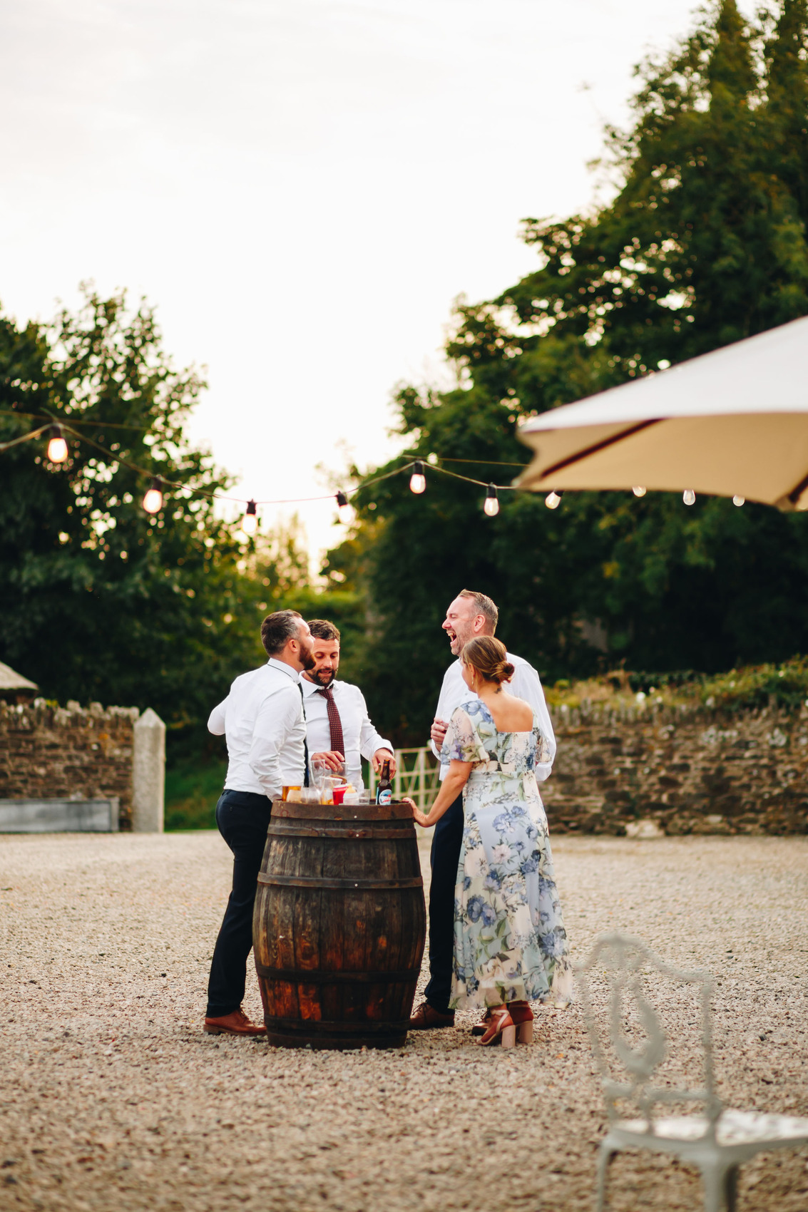 Wedding guests laughing stood in a courtyard by a barrel