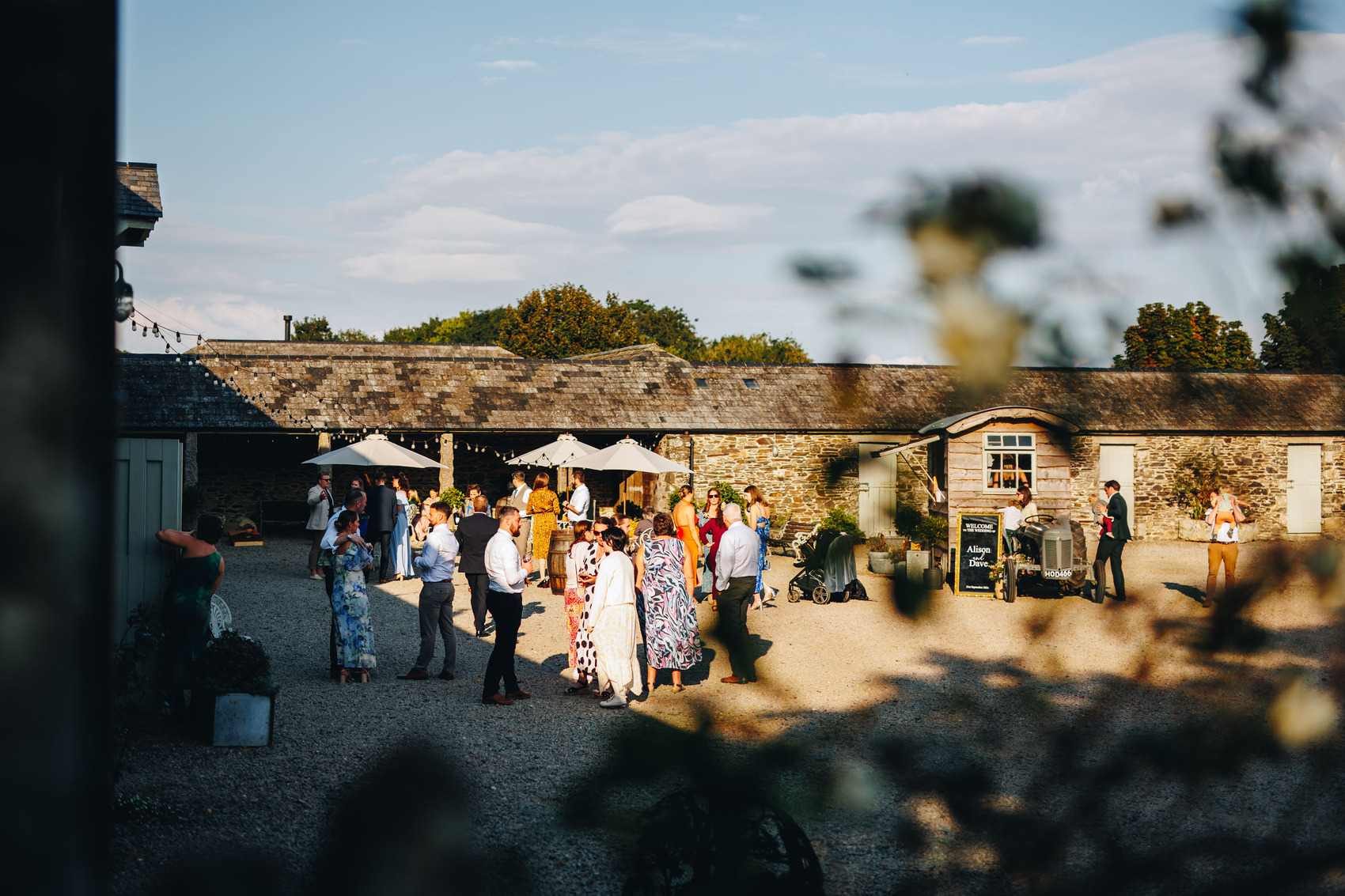 Evening sunshine and guests mingling in courtyard with foliage in the foreground