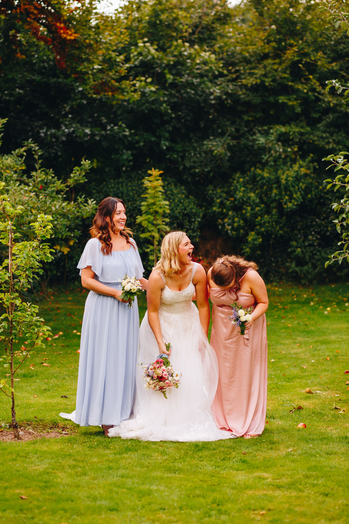 Bride and two bridesmaids stood in gardens, laughing