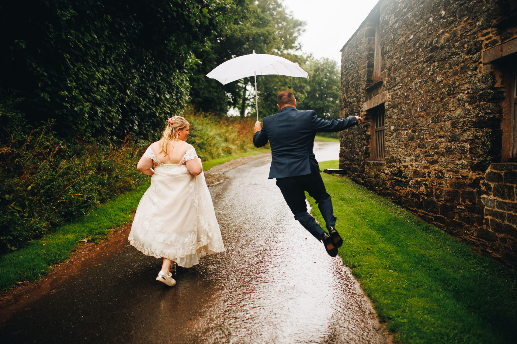 Couple running/jumping, running up a track to Bradstone Manor Weddings in the rain