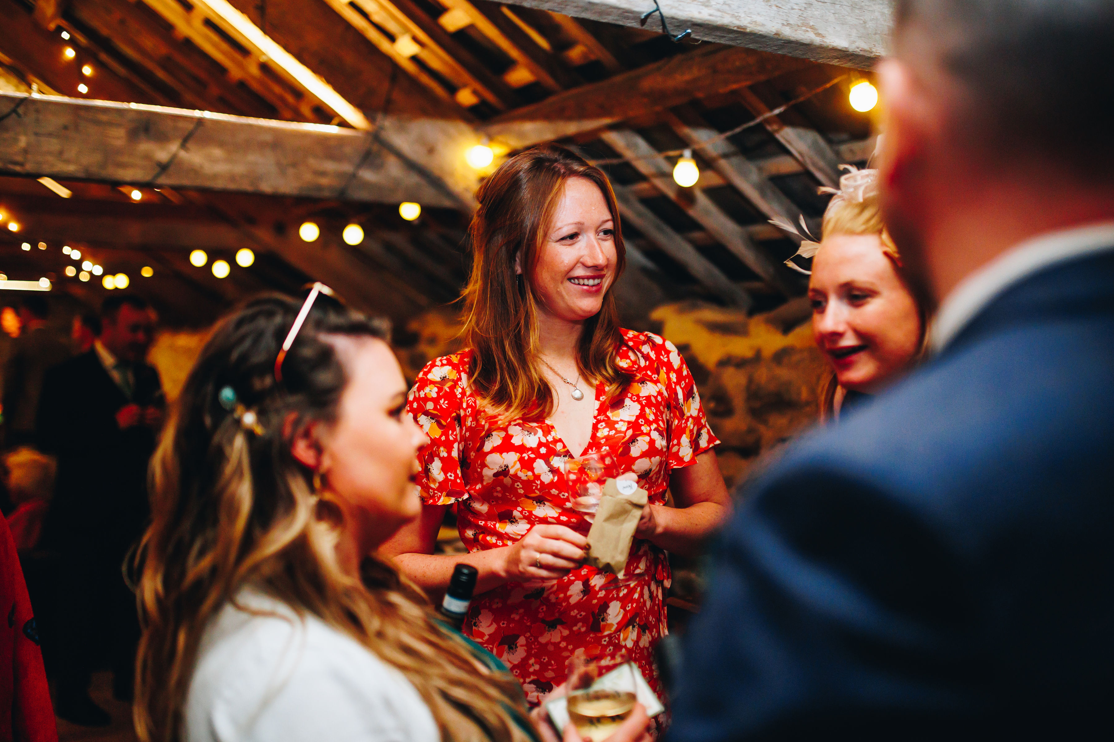 Wedding guests smiling and chatting in a fairy lit room with beams