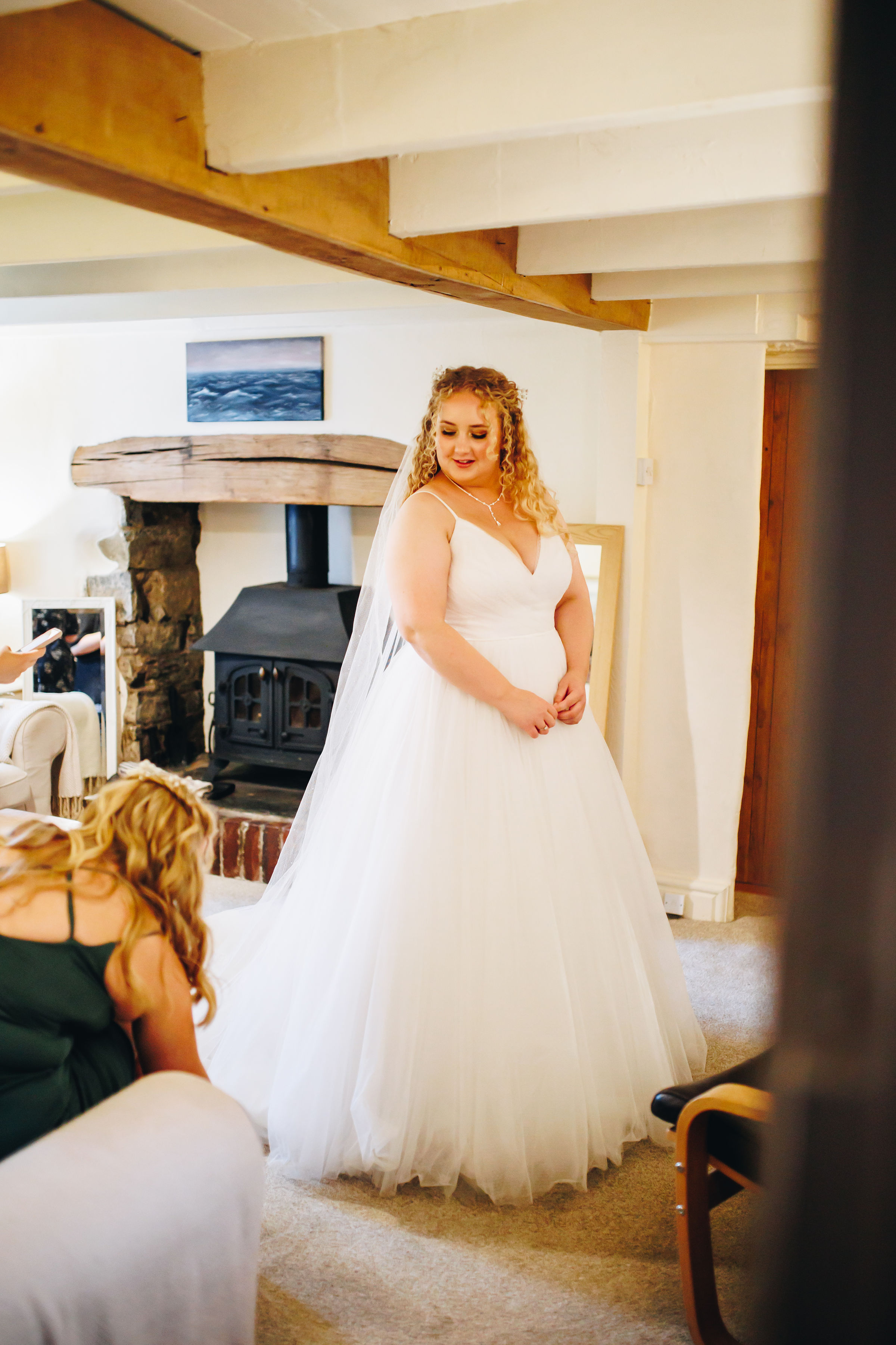 Bride stood in the lounge while sister sorts out the bottom of her dress