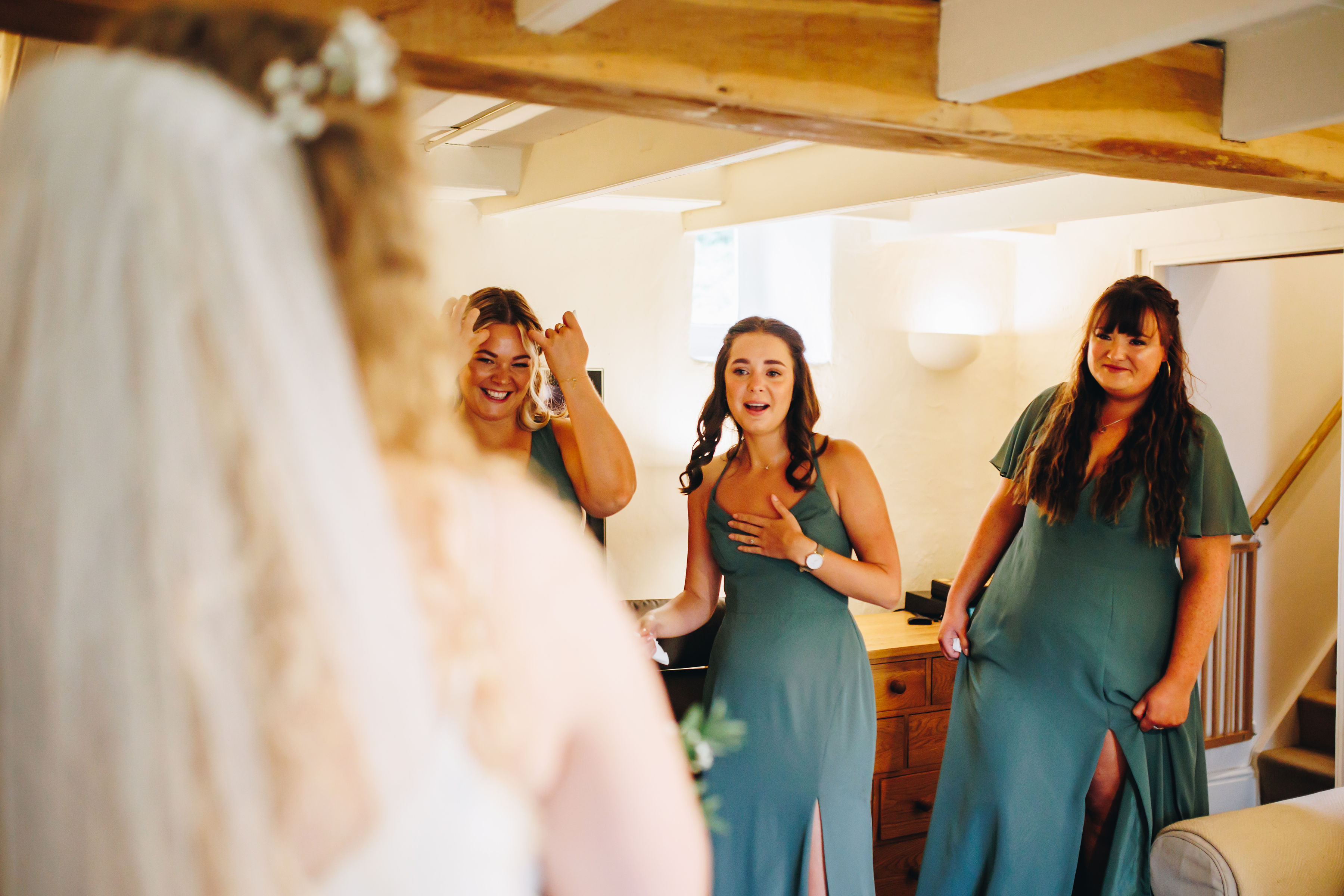 Bridesmaids in teal dresses tearing up after seeing the bride all dressed up