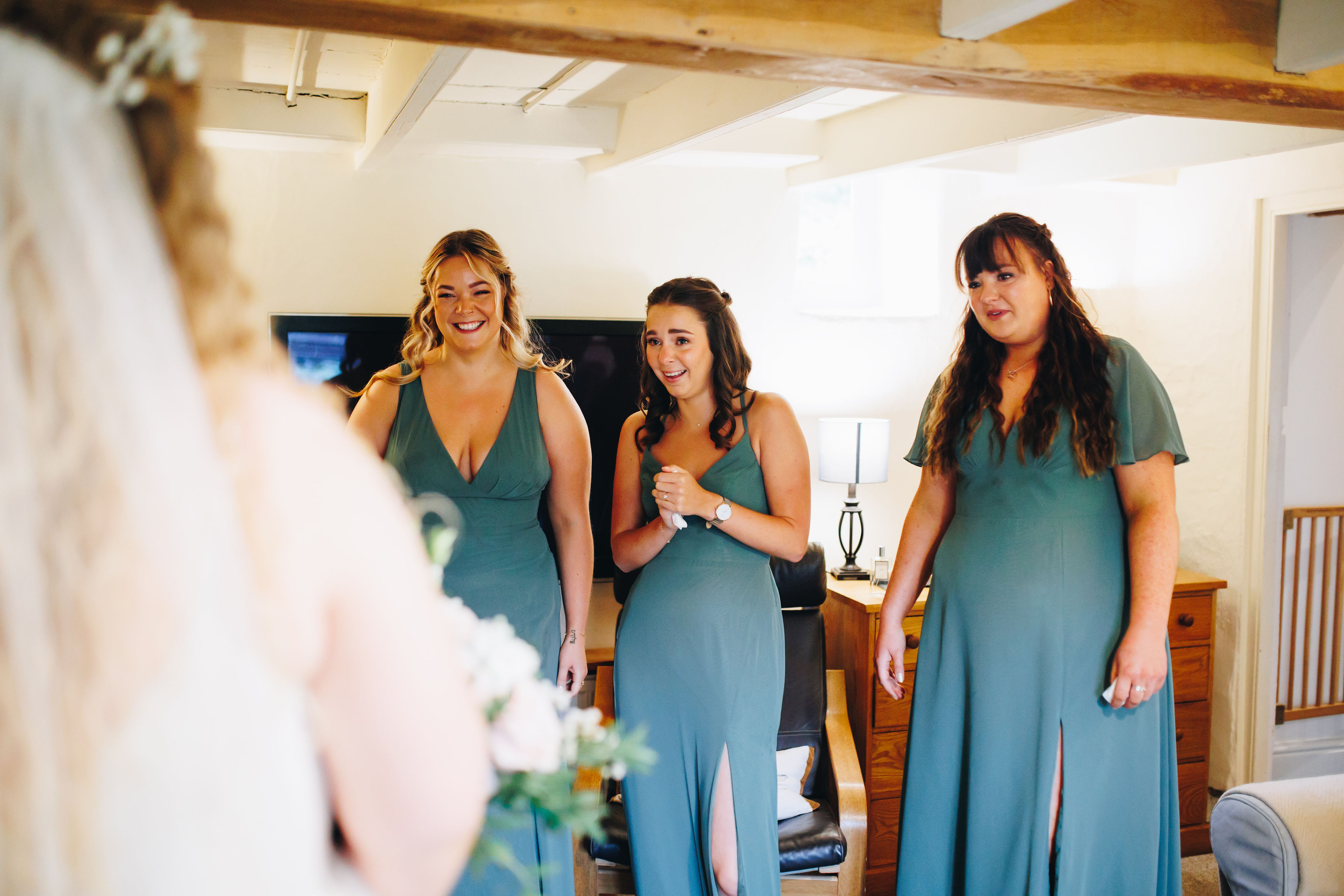 3 bridesmaids in teal dresses tearing up when looking at the bride, in the foreground