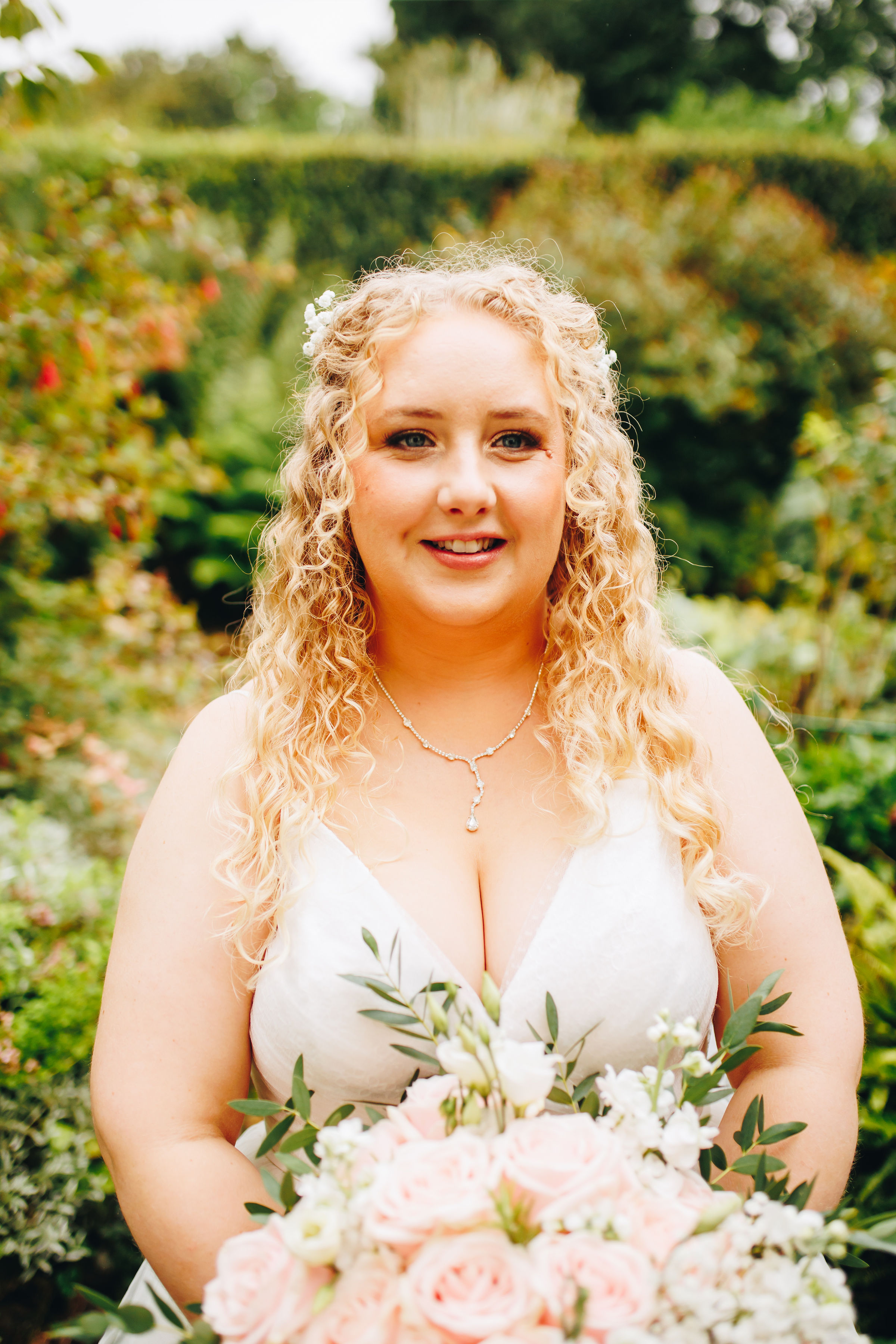 Bride smiling, looking off-camera and holding a bouquet, in a garden