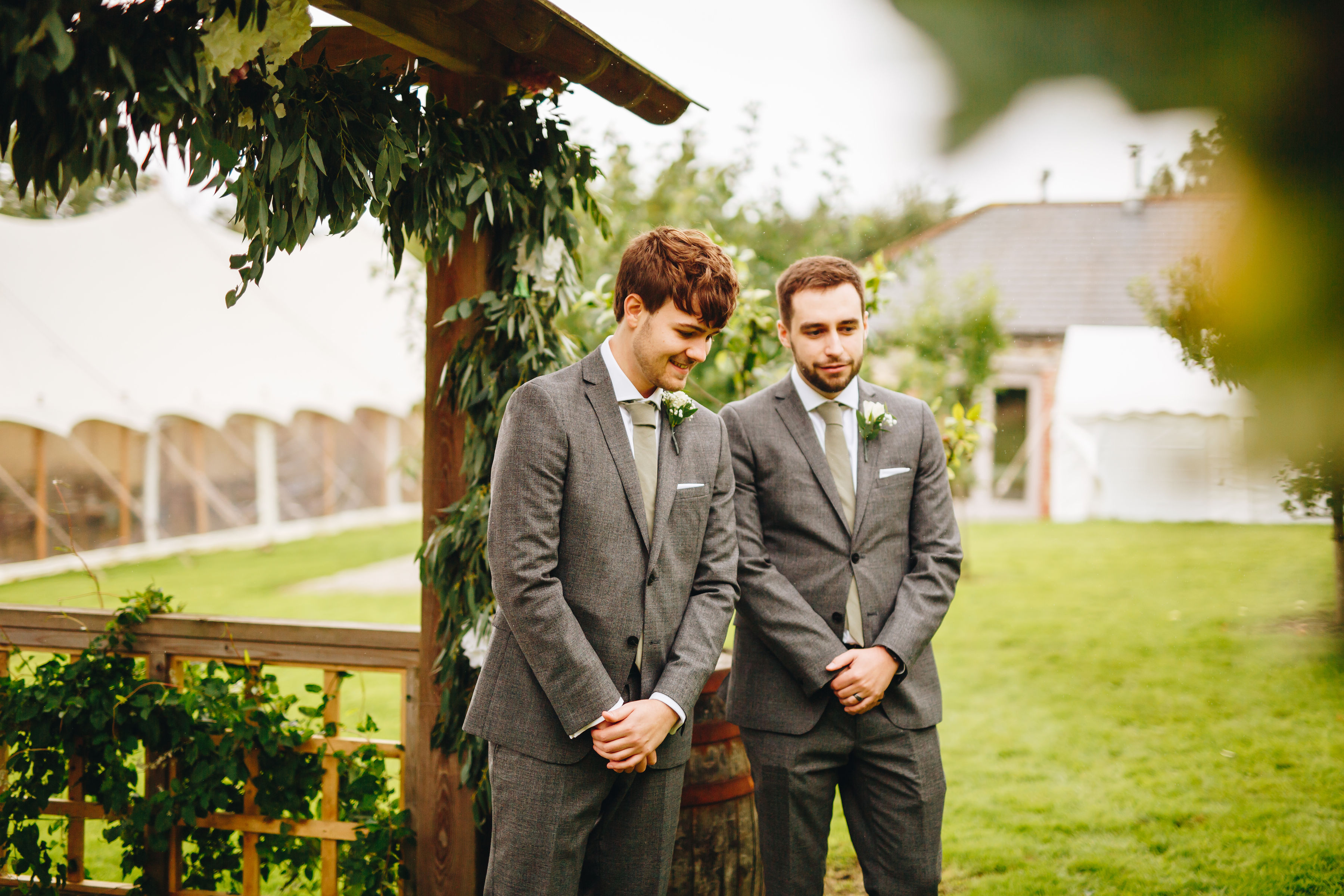 Groom and best man stood waiting by a wooden structure