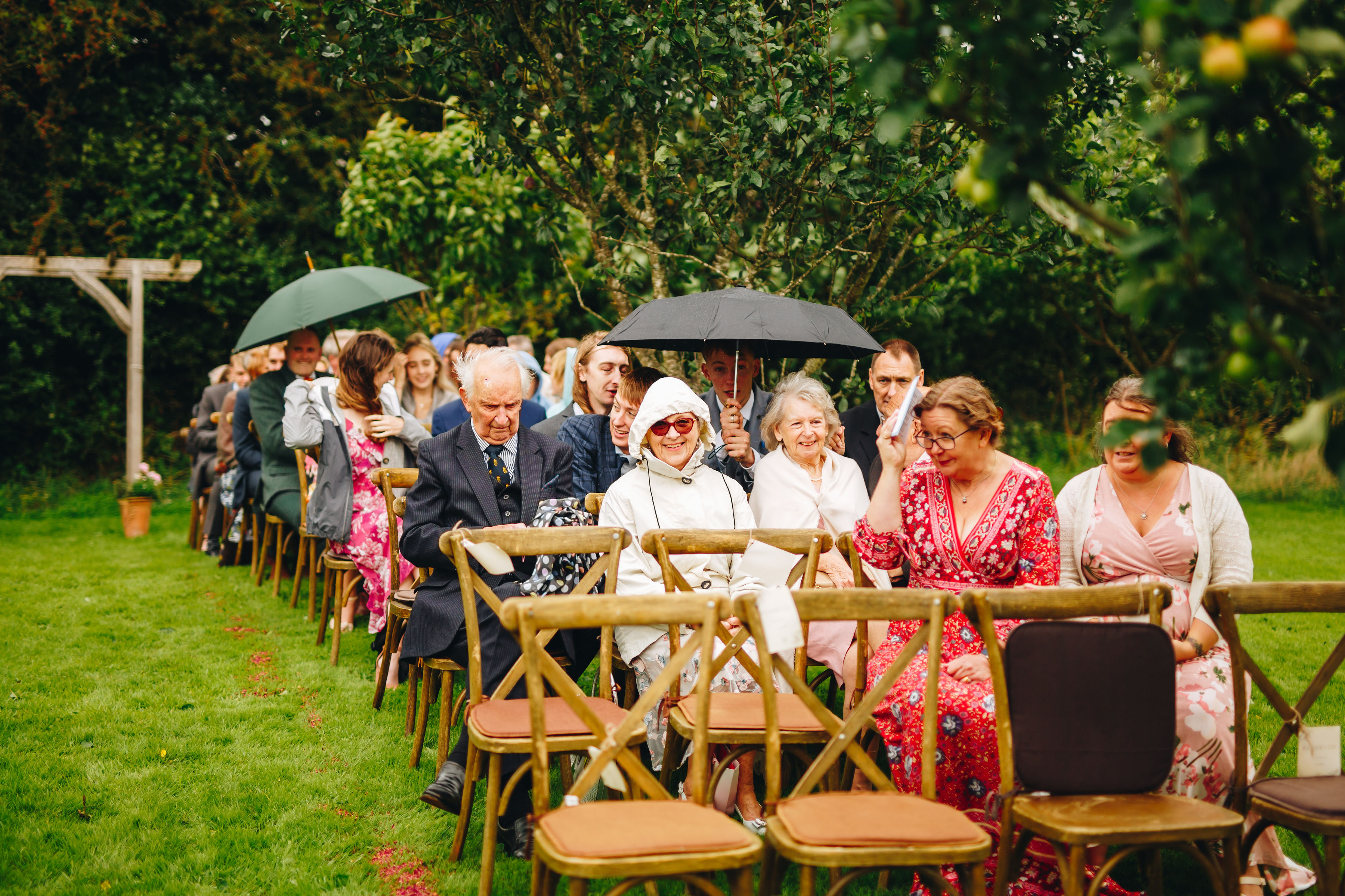 Wedding guests sit with umbrellas and hoods up