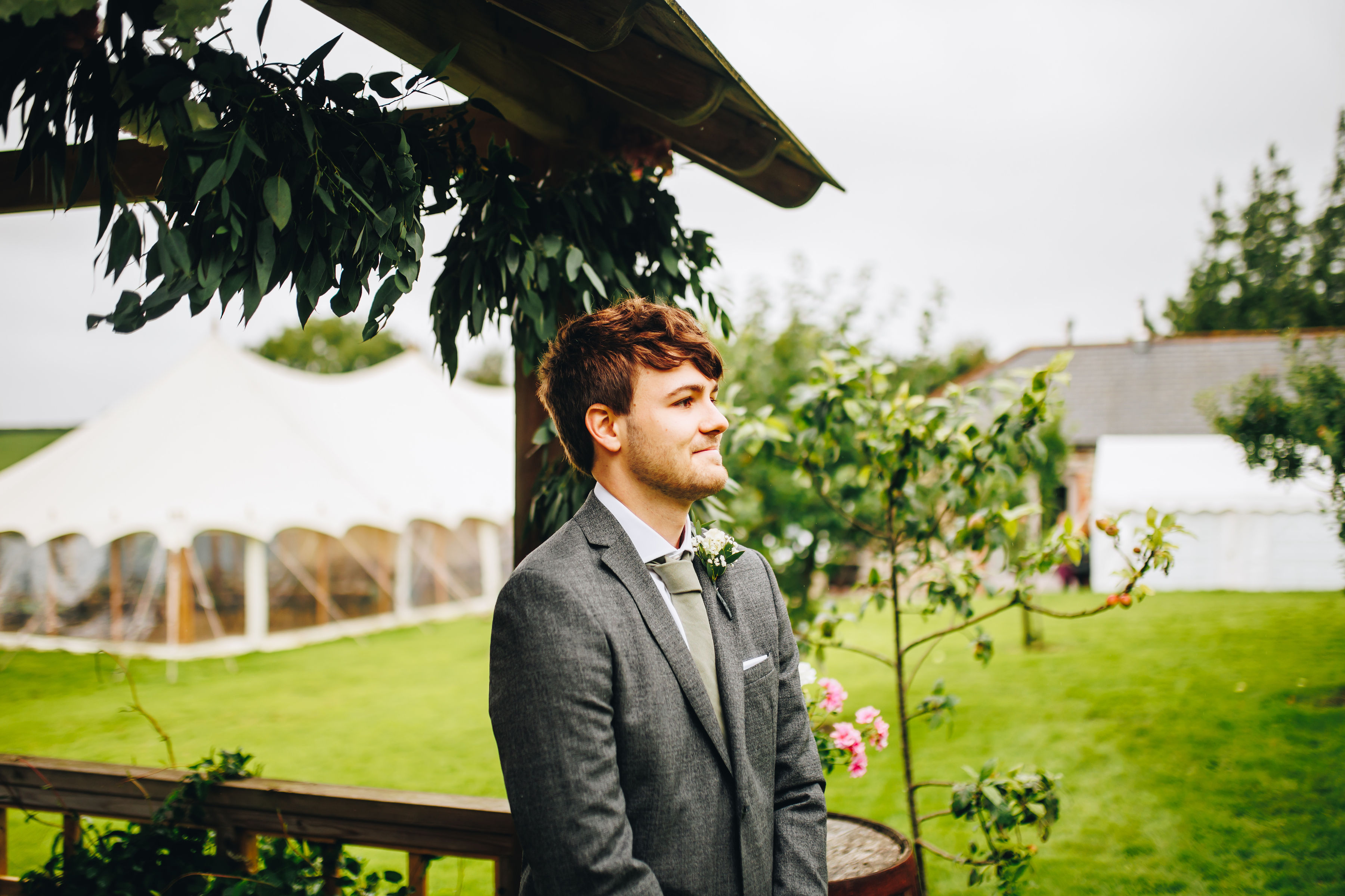 Groom waits excitedly, stood under a wooden structure with plants everywhere