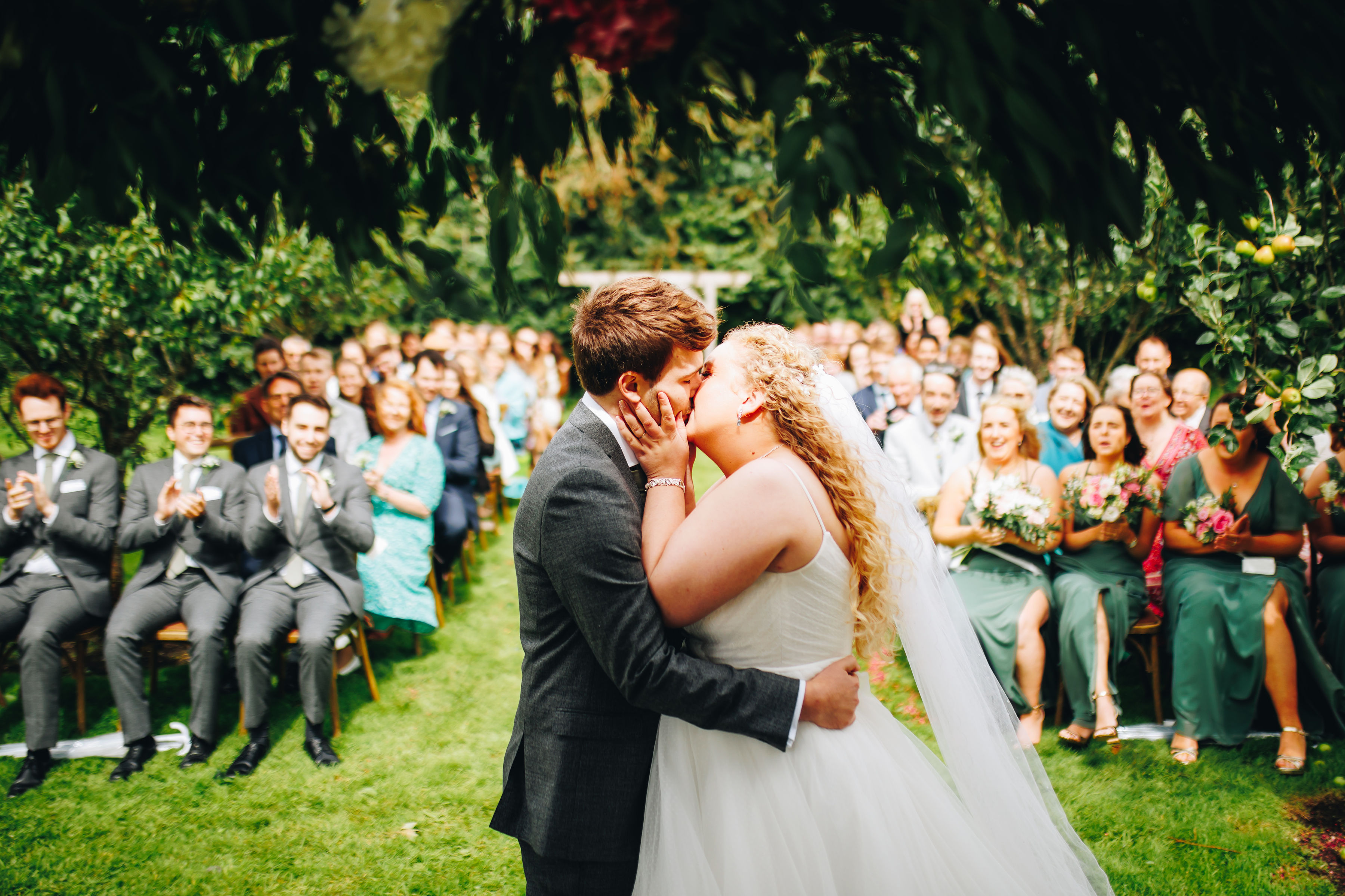 Bride and groom stood holding having their first kiss at their wedding ceremony
